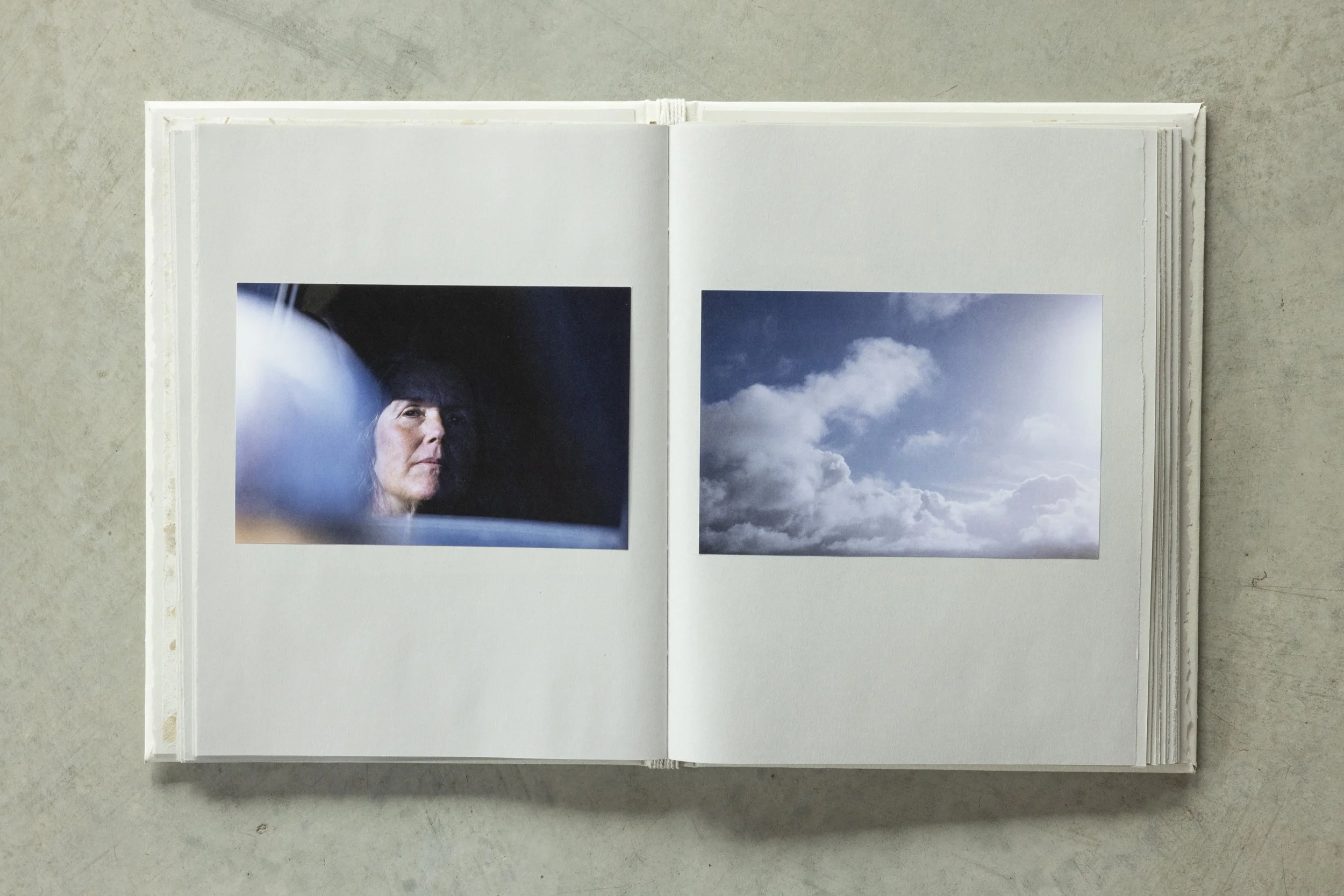 Open photo album with two pages displaying pictures of clouds and a woman’s face reflected in a mirror.