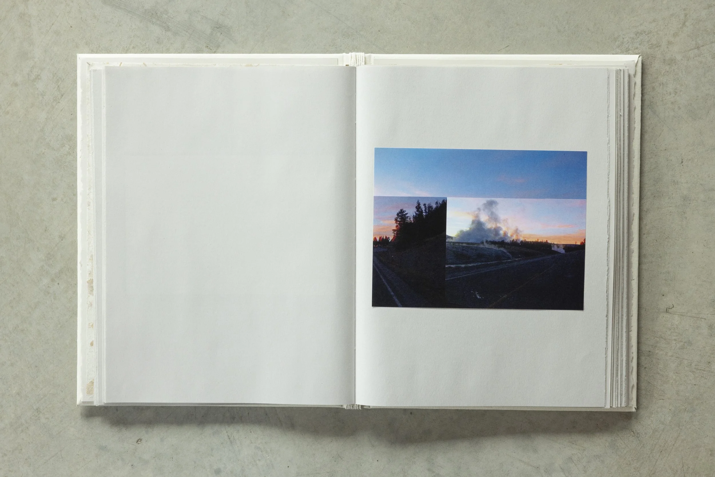 Open white photo album on a gray surface, showing a double page with a collage of four landscape photographs of a sunset over a beach with trees and clouds.