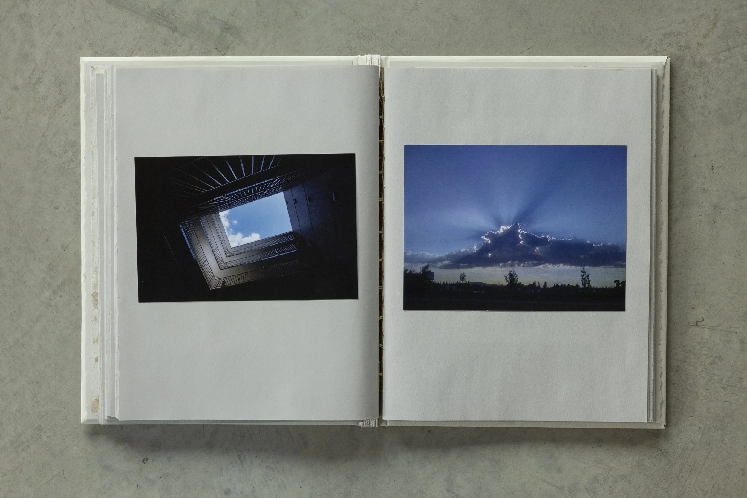 Open photo album with two pages showing landscape photographs, one of a building viewed from below and another of a cloudy sky with sunlight.