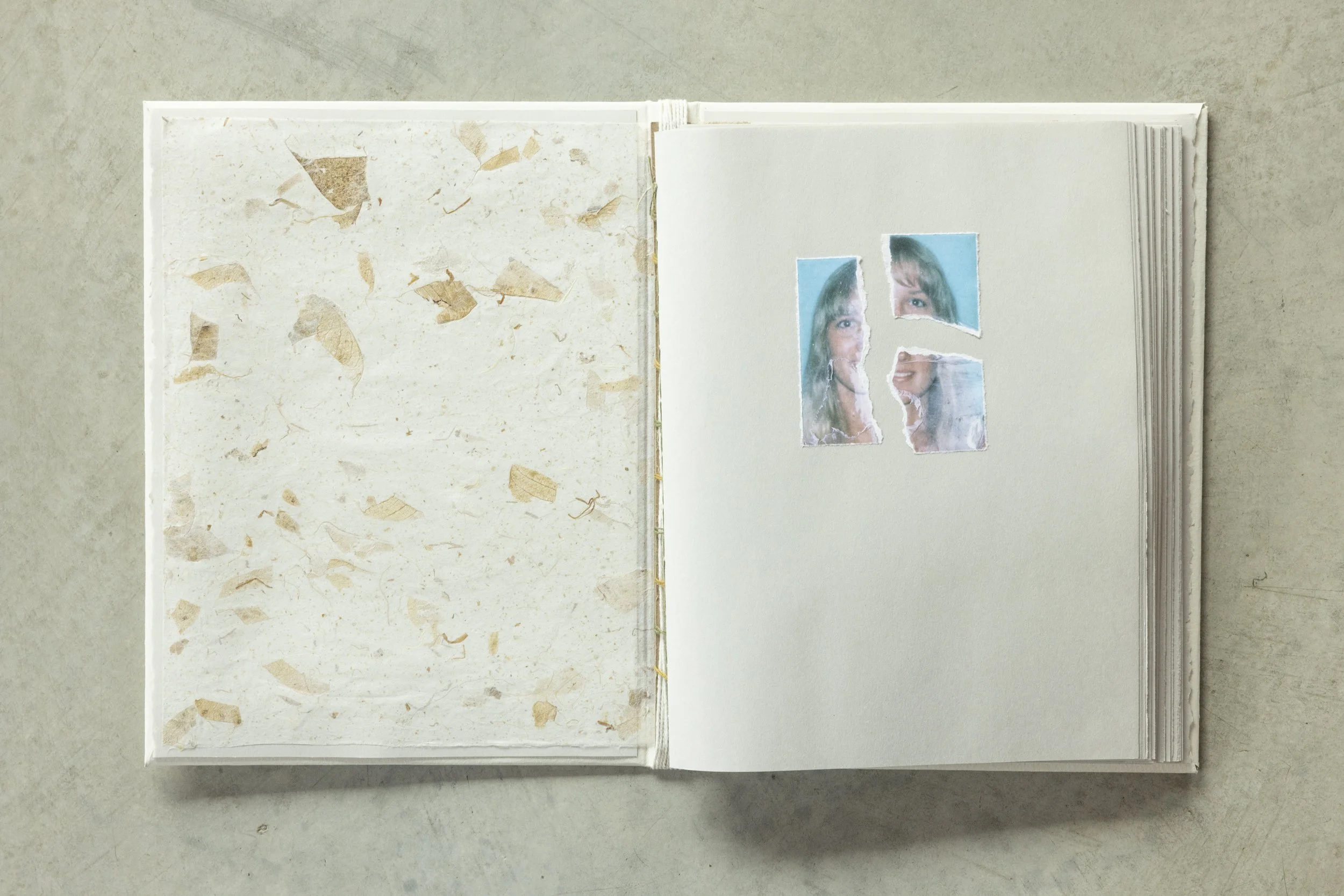 An open scrapbook containing two pages. The left page has a textured background with torn paper pieces, and the right page has three torn photo pieces of a woman's face with a light blue background.