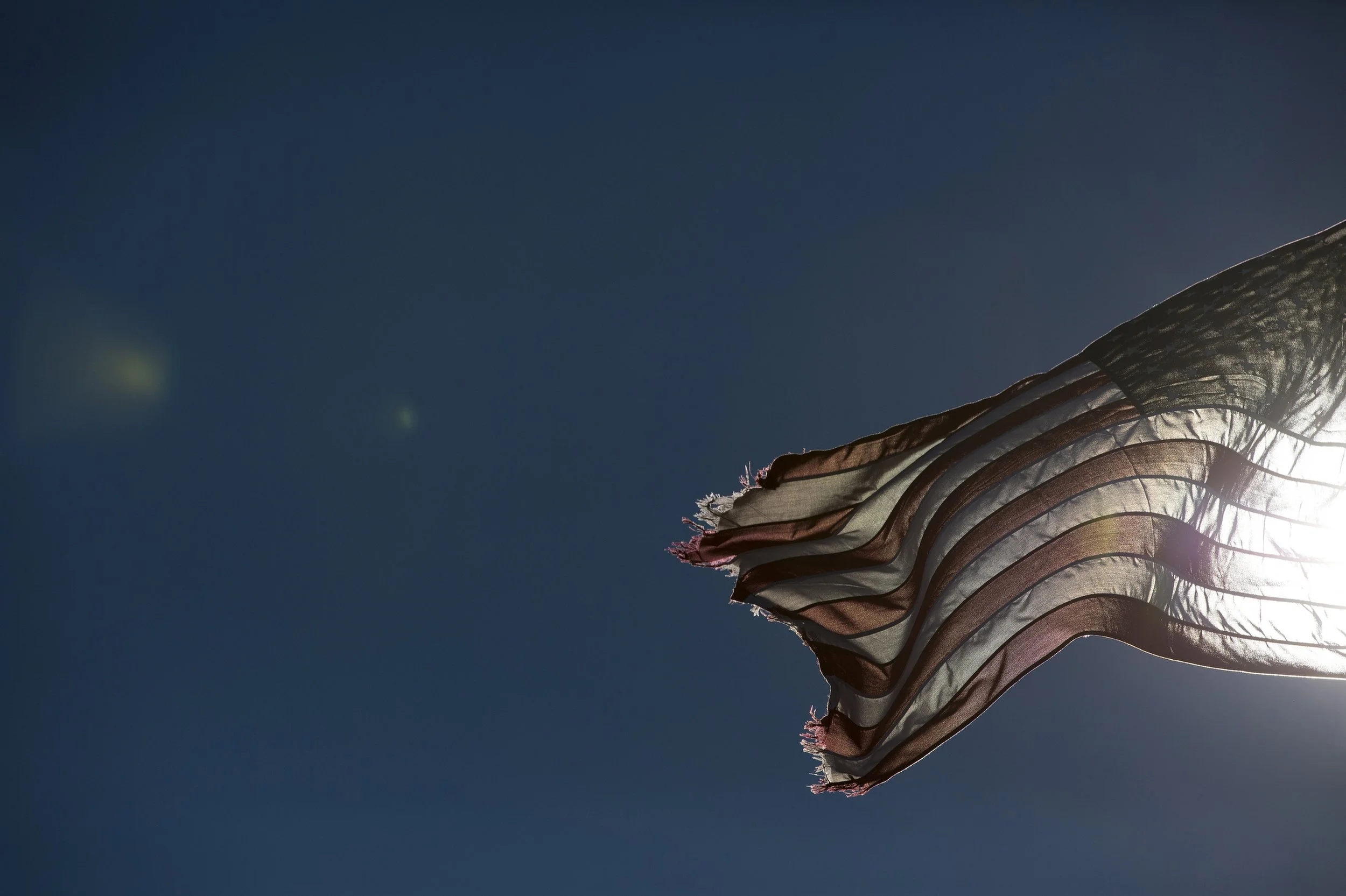 American flag waving in the wind against a bright sun and blue sky.