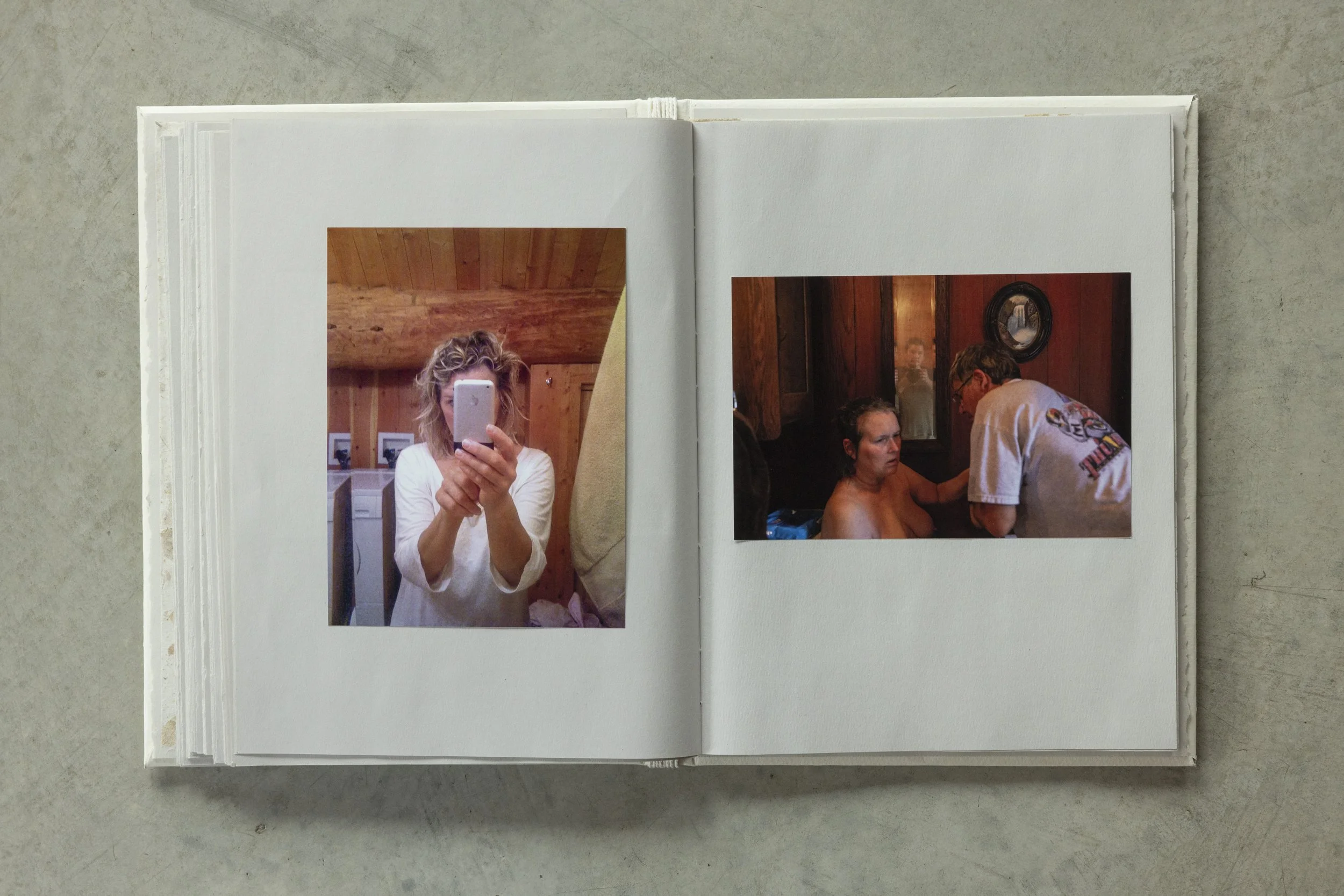 Open photo book with two photographs of people taking selfies and engaging in a conversation, on a gray surface.