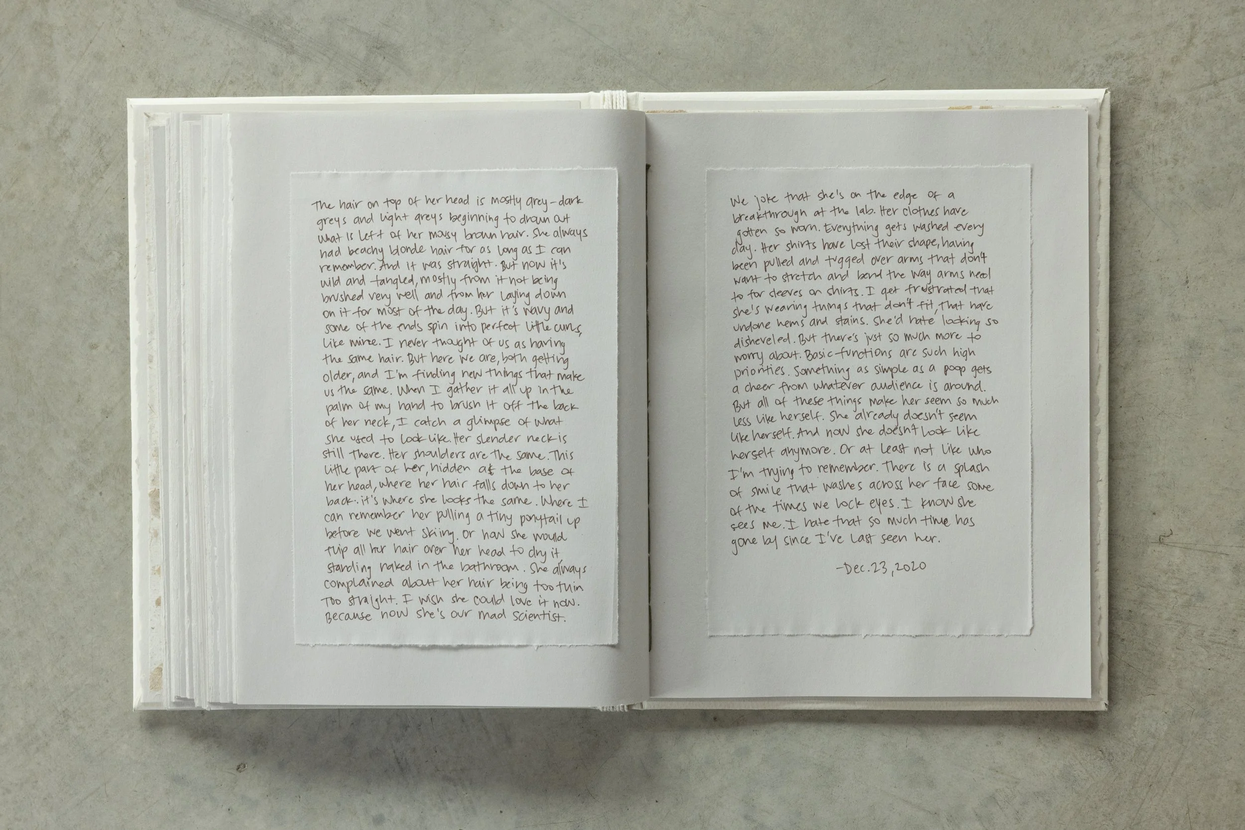 An open book placed on a concrete surface, showing handwritten text on both pages.