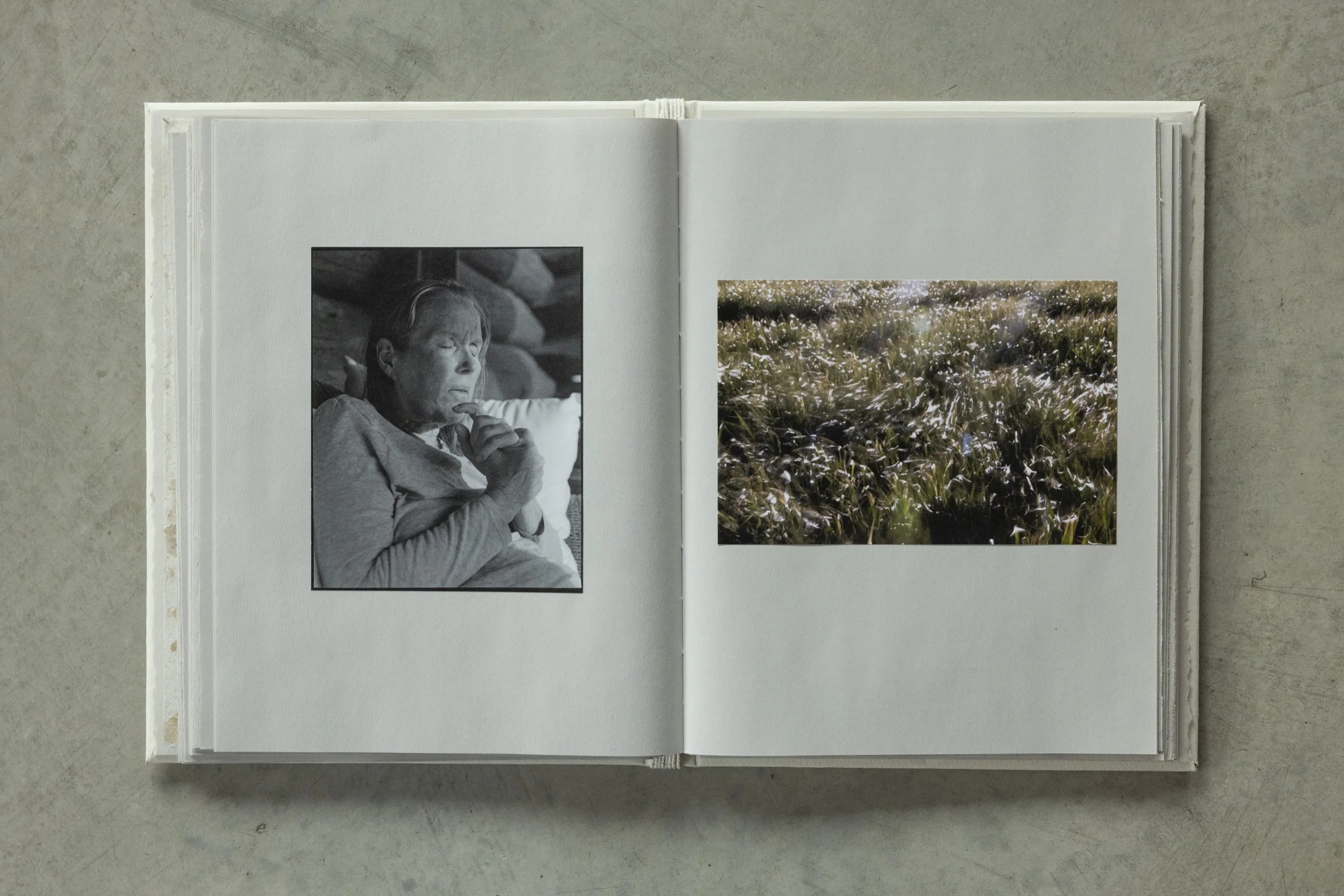 Open photo album with black and white picture of an elderly woman with short hair and closed eyes, and a color photograph of a field of flowers with light reflecting off them.