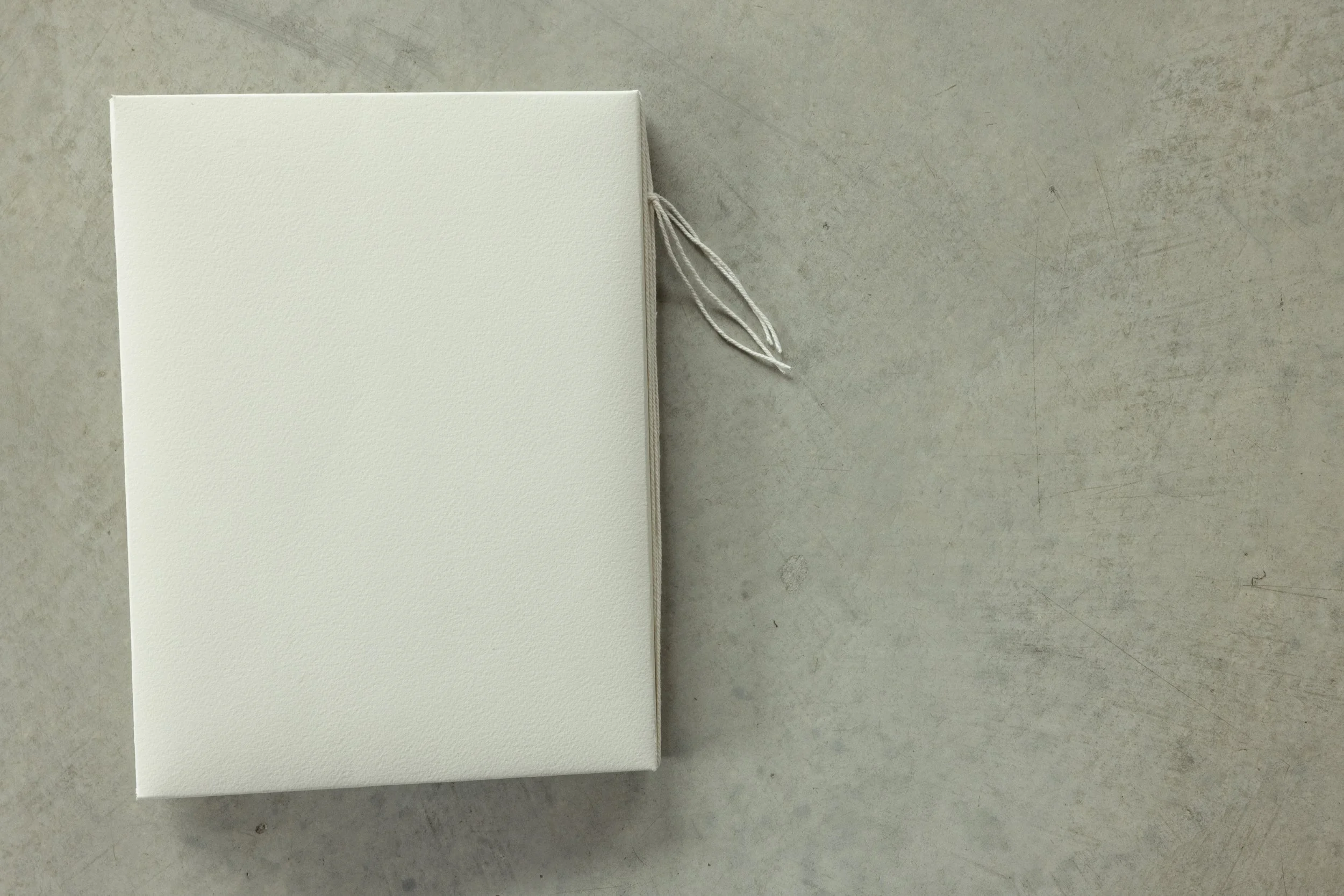 A closed white textured box with string ties, placed on a beige surface.