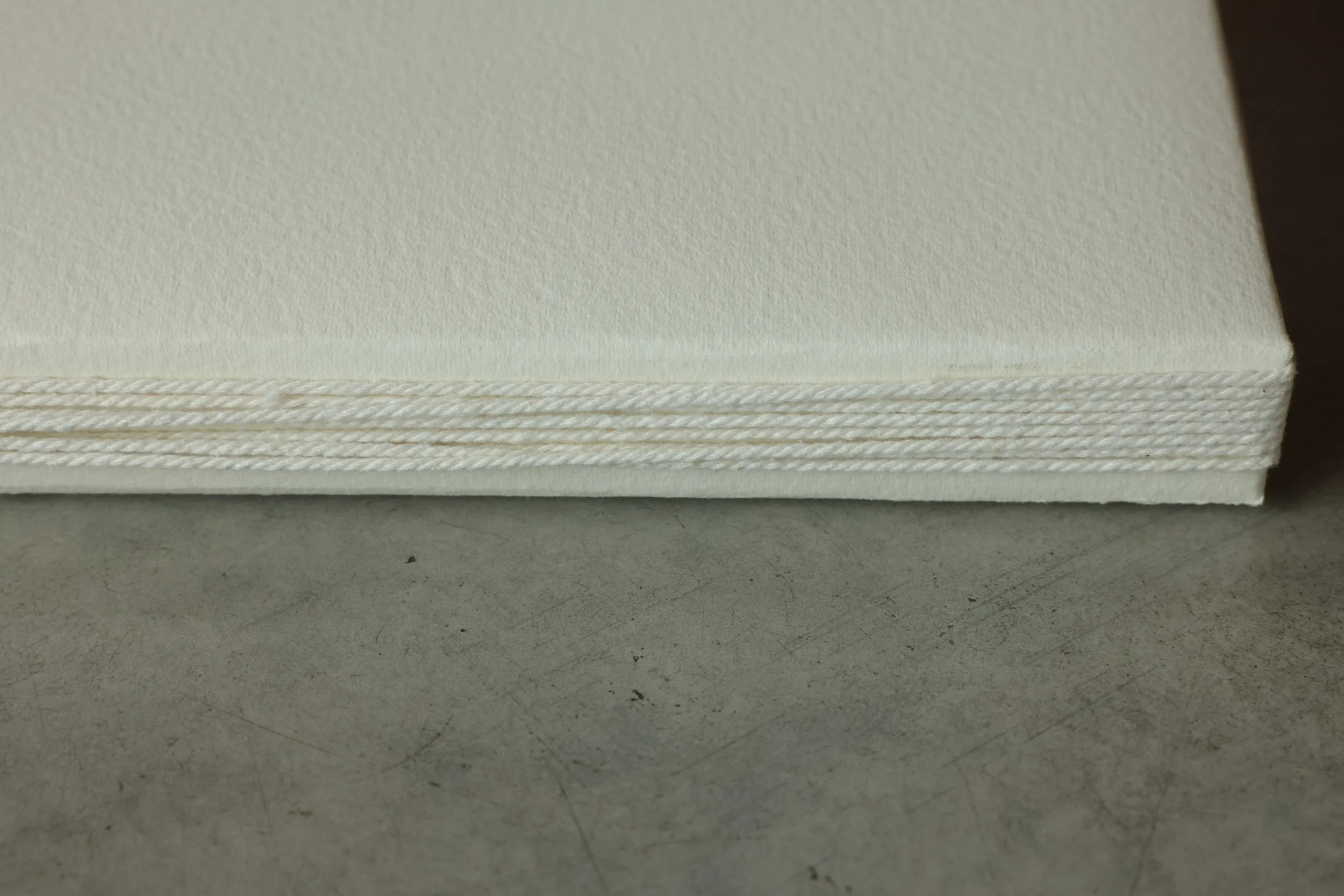 Close-up of a stack of white paper napkins with a twisted cord border placed on a gray surface.