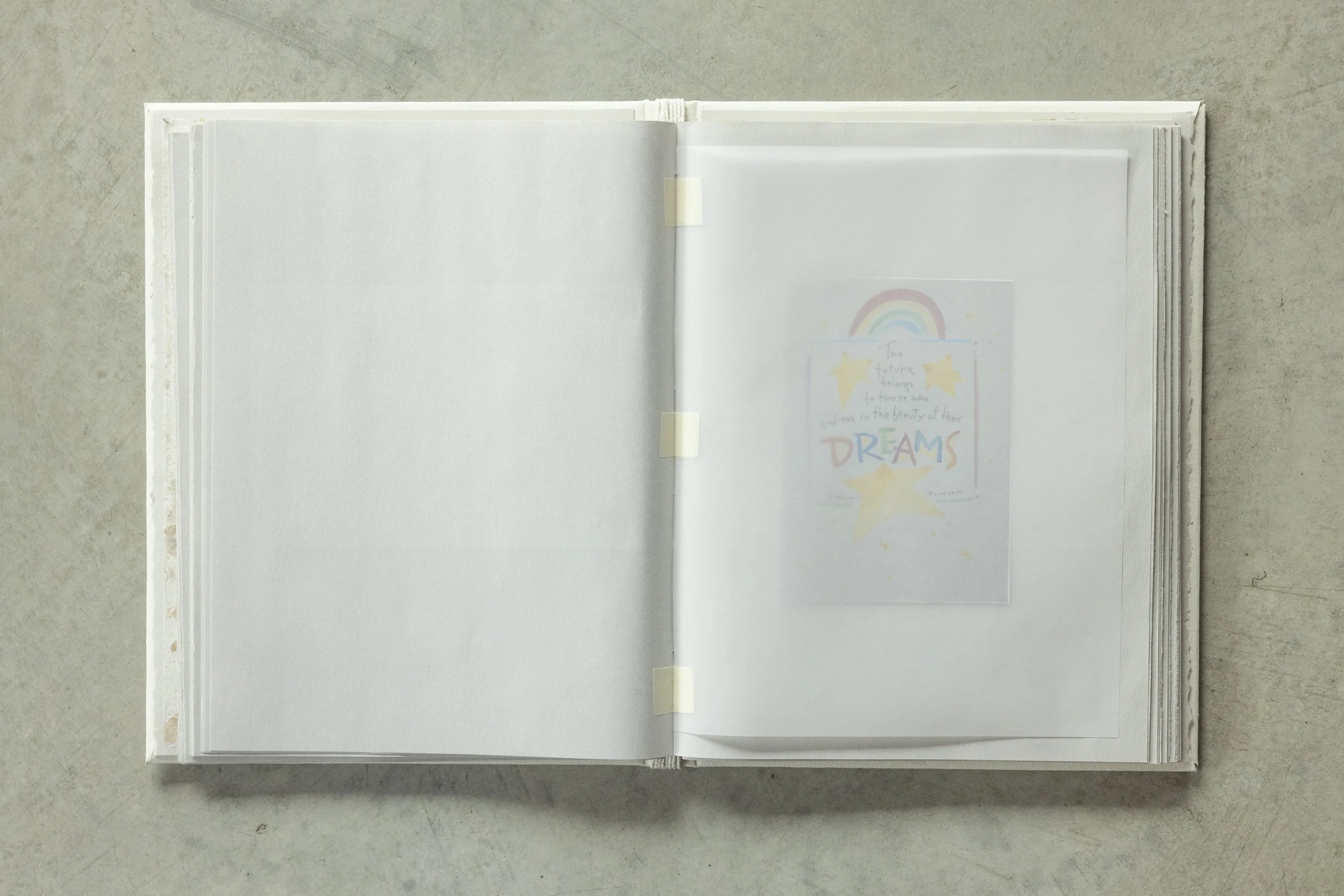 Open scrapbook or album with blank pages and colored artwork on the right page, resting on a concrete surface.