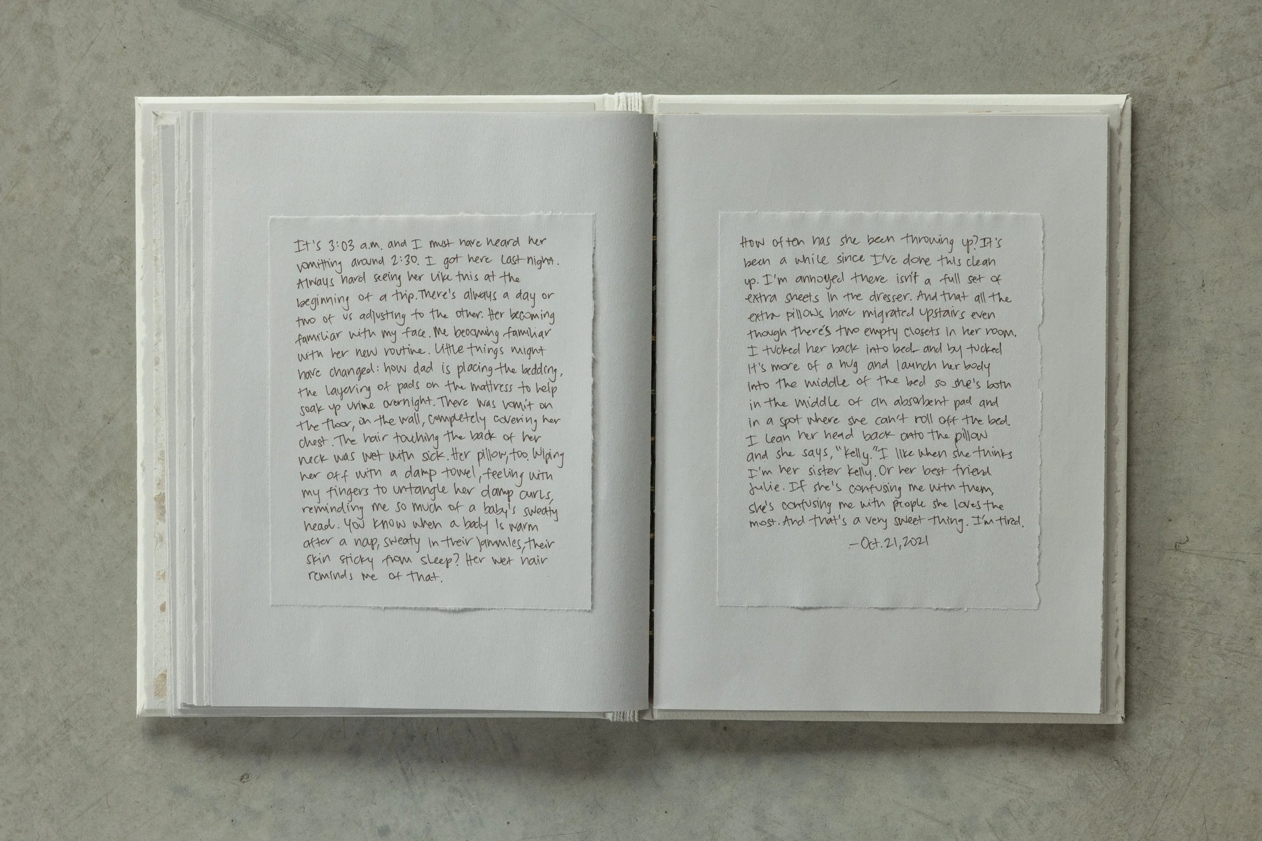 Open notebook with handwritten text on two pages, placed on a concrete surface.