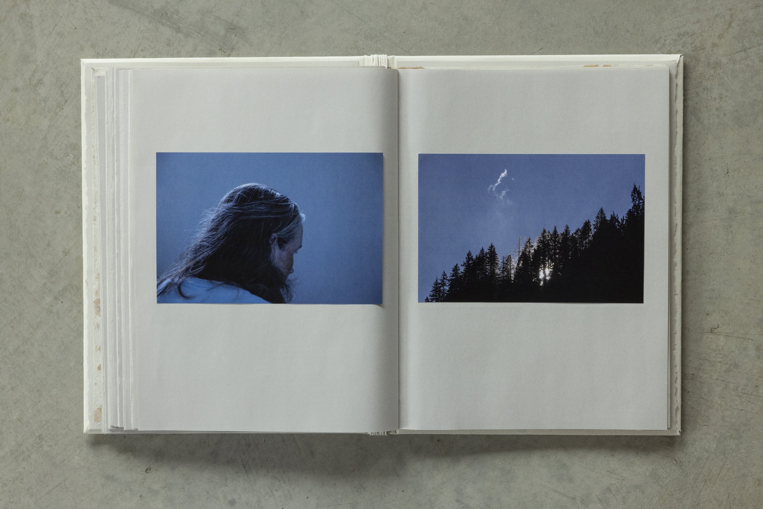 Open photo album showing two photographs; one of a woman with long hair and a blue top, and another of a forested mountain landscape with a cloudy sky above.