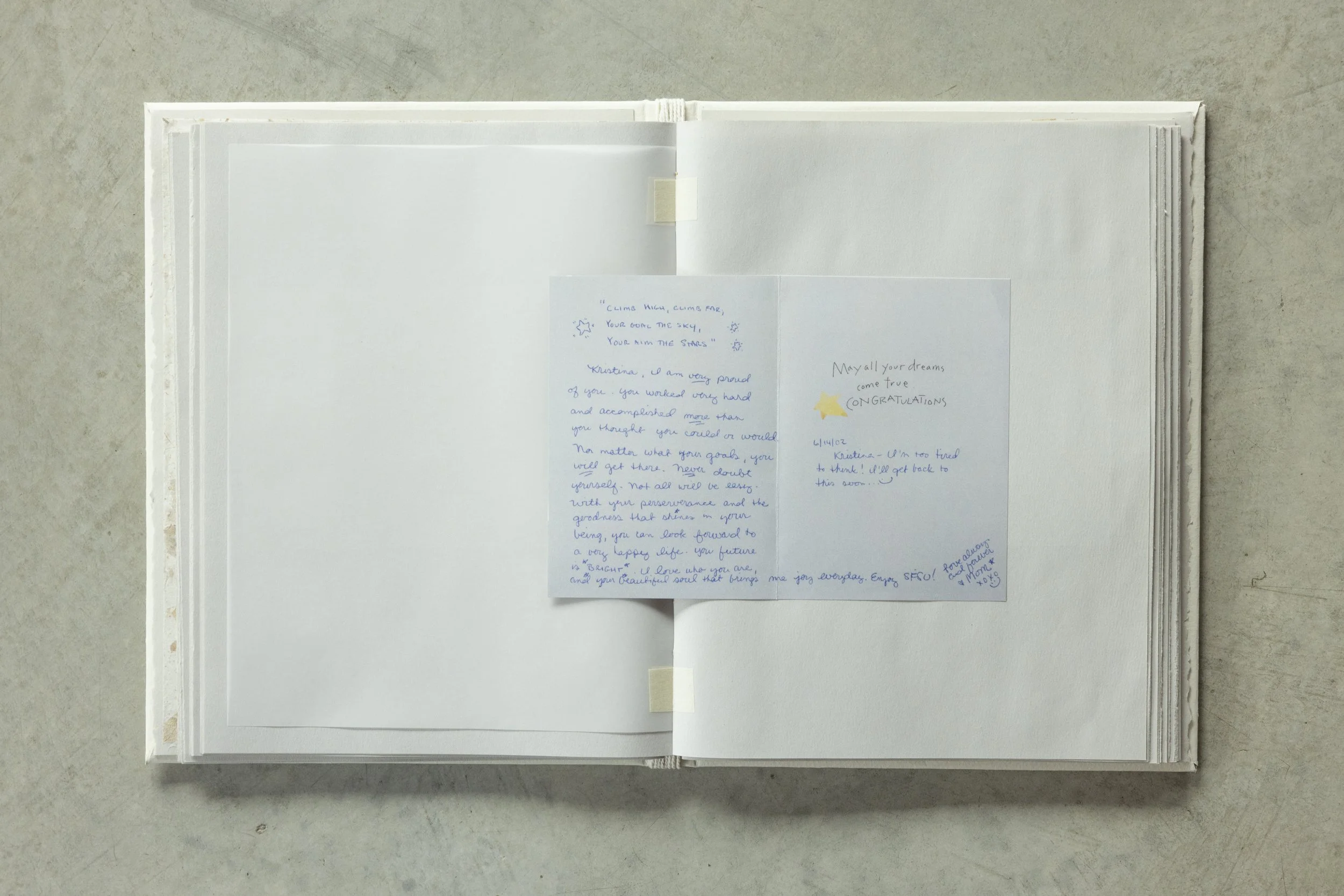 Open white cardboard photo album with handwritten notes and small decorative stars on handwritten notes inside, placed on a light-colored surface.