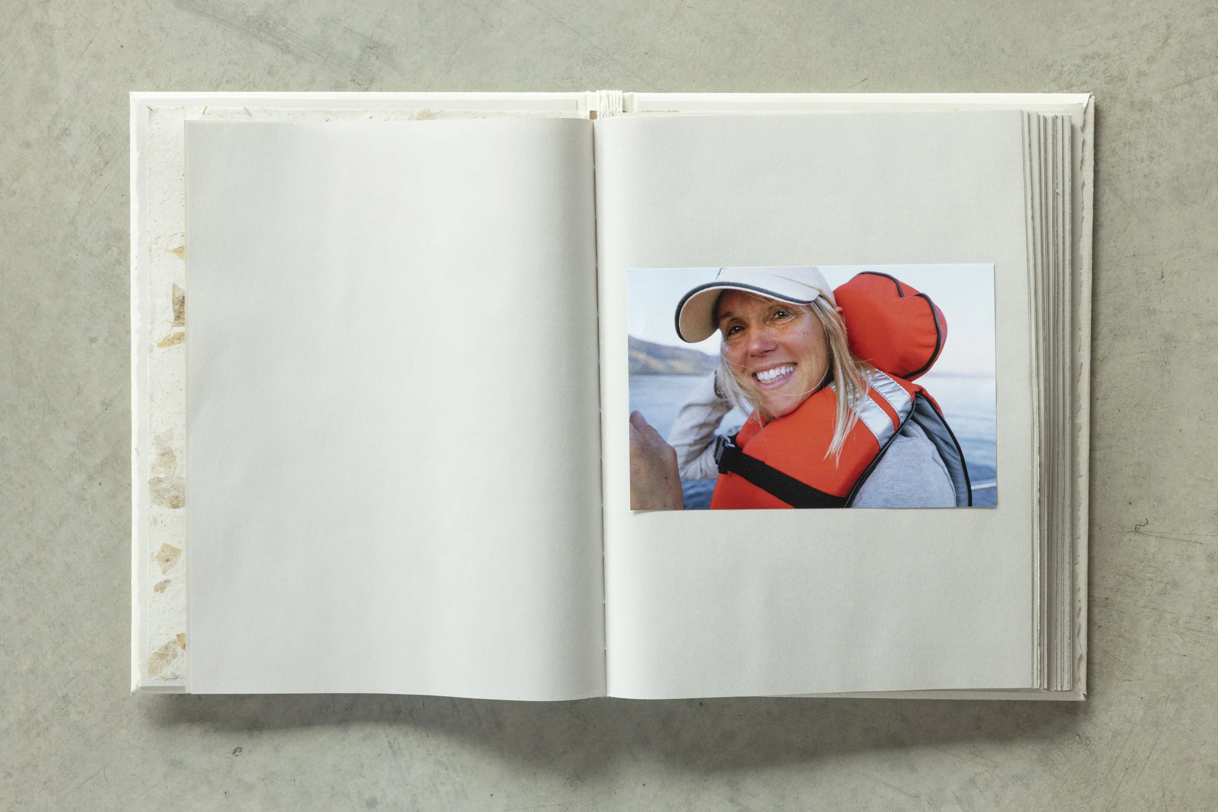 An open blank scrapbook with a printed photo of a smiling woman in outdoor gear, including a cap and life jacket, affixed to the right page.