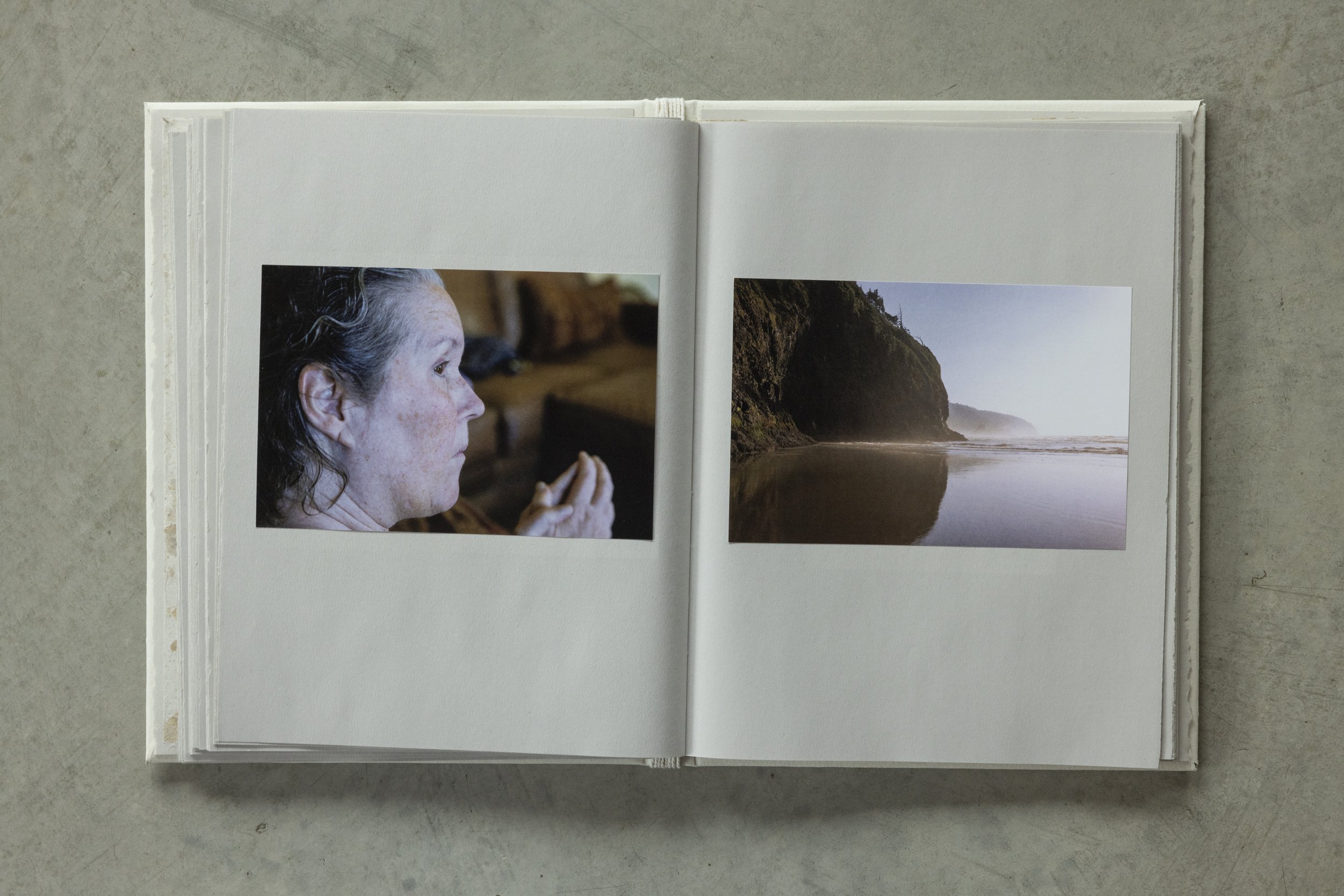 Open photo album containing a portrait of a woman with long dark hair and freckles, and a landscape photo of a rocky coast with a body of water and fog in the distance.