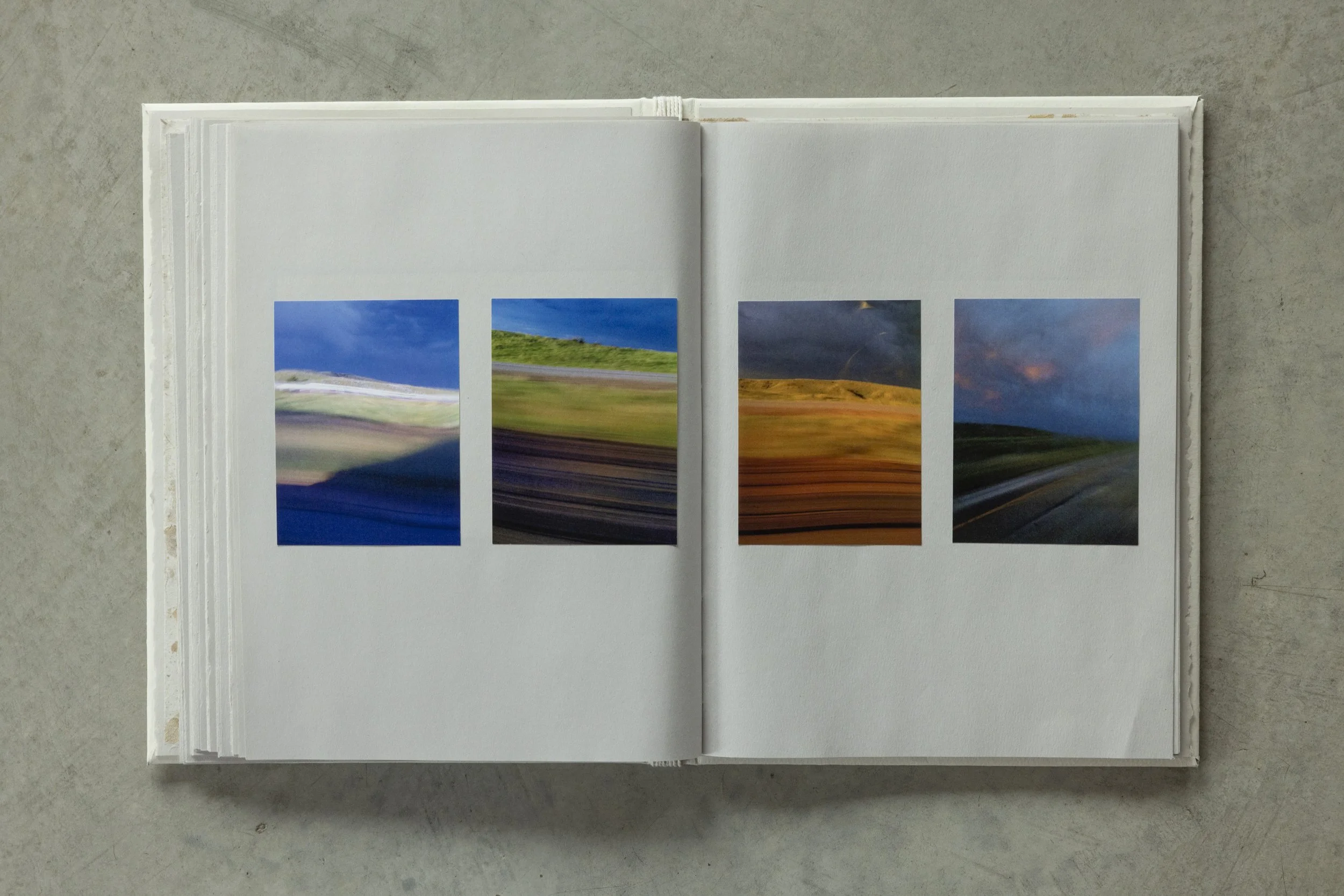Open book with abstract landscape photos on a white background, laid on a gray surface.