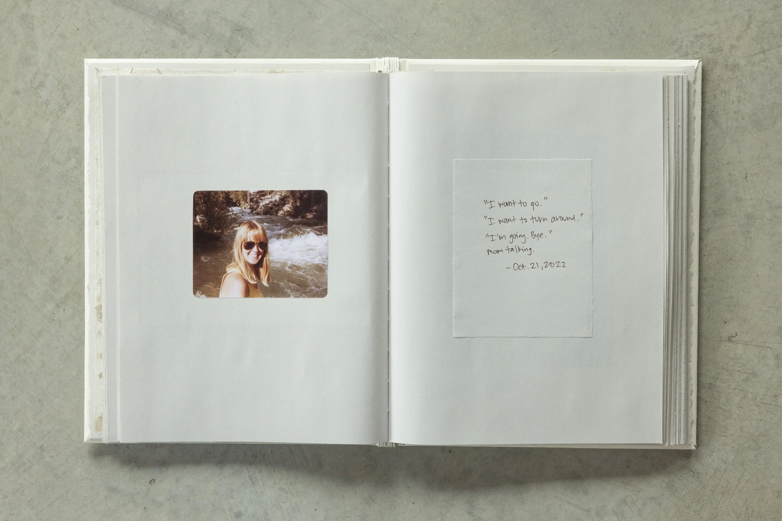 Open photo album with a picture of a young woman wearing sunglasses near a river and a handwritten note with dated message.