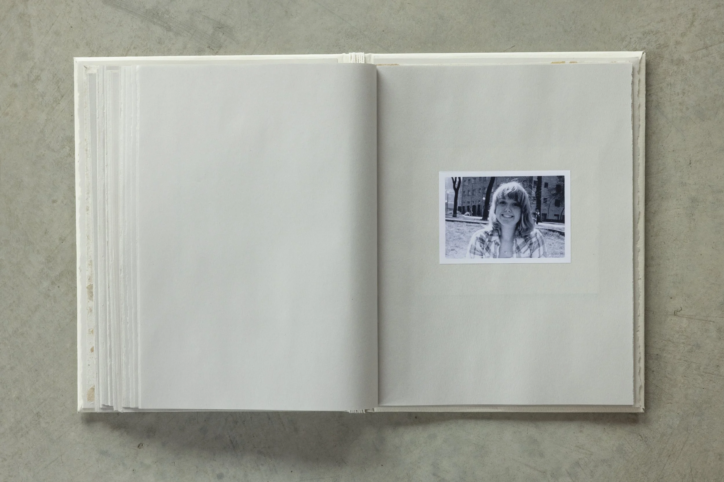 Open blank photo album with a black and white photo of a smiling girl with shoulder-length hair, standing outdoors in a city park.
