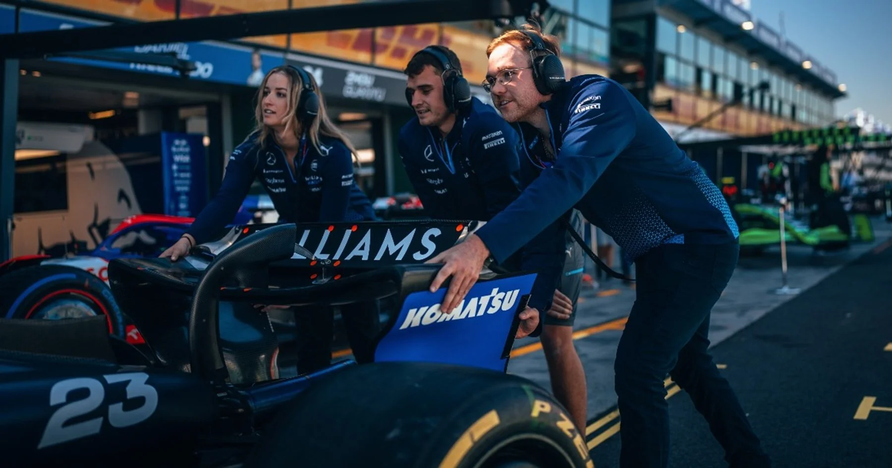 Komatsu apprentices standing in front of a Williams Racing F1 car in the pit lane