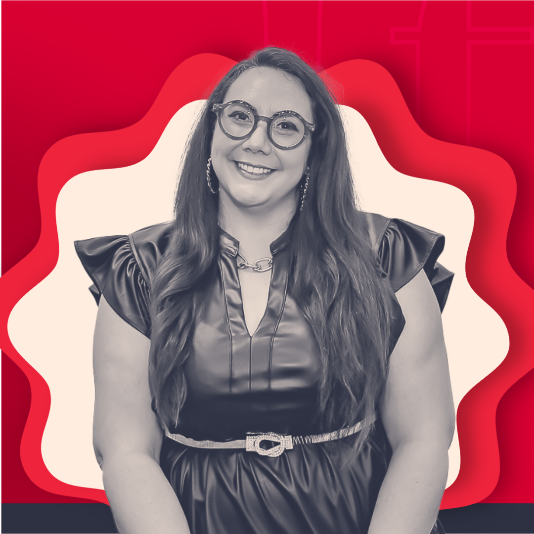 A woman with glasses, long wavy hair, and earrings smiling at the camera, wearing a shiny black dress with ruffled sleeves and a chain necklace, in front of a graphic background with red, white, and black abstract shapes.