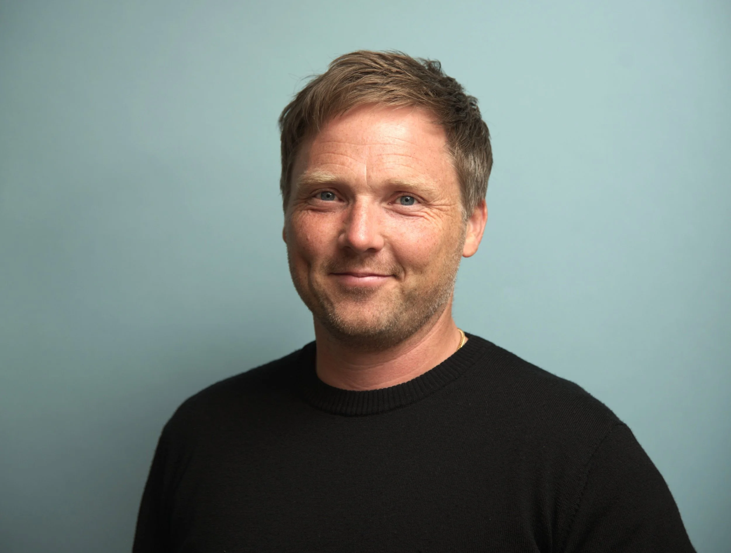 Man i blå tröja mot blå bakgrund, leende.