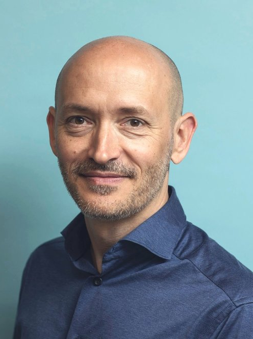 Man i blå skjorta mot ljusblå bakgrund.