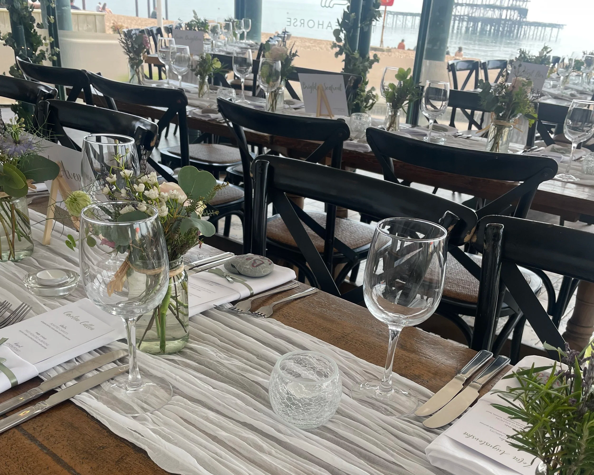 A beautifully set dining table with glassware, flowers, menus, and silverware, overlooking a beach and ocean view.
