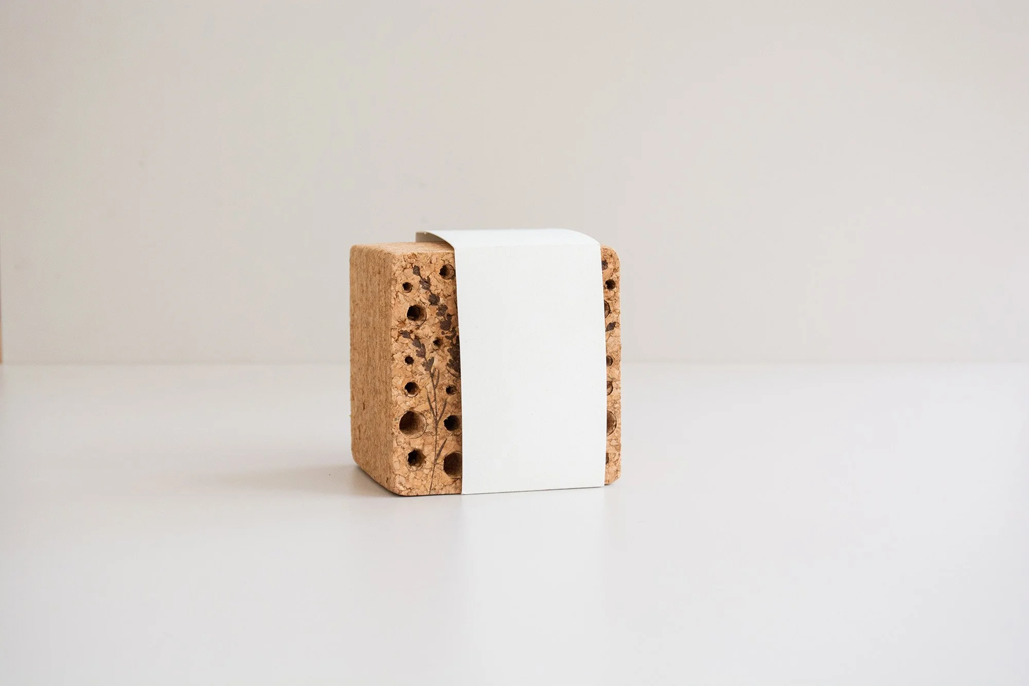 Caja de madera con forma de casa y tubos de diferentes tamaños, rodeada de paja y sobre fondo neutro.