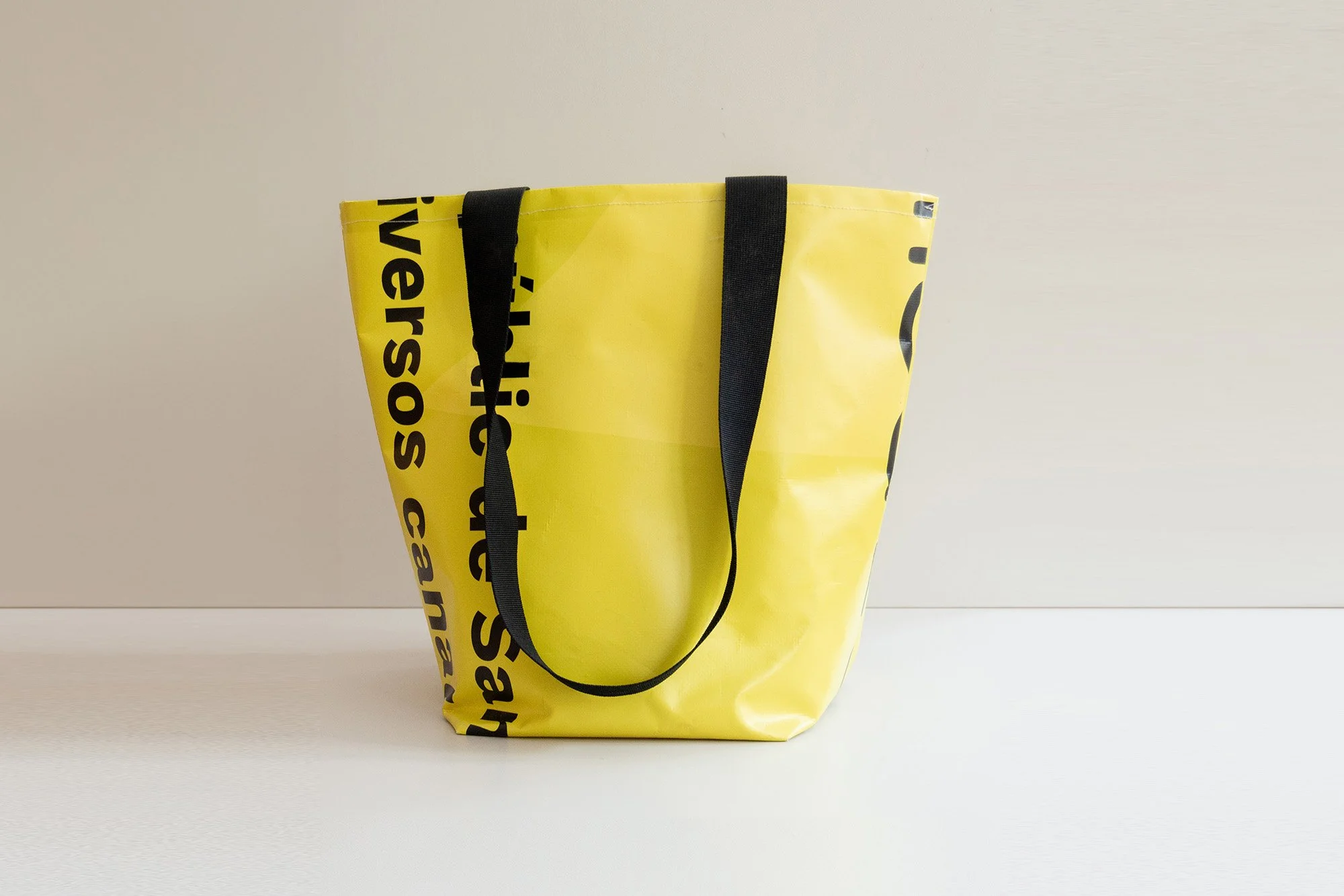 Bolsa de tela blanca con diseño de árboles y montañas, con la frase 'Not all those who wander are lost' y un espacio para un logo personalizado en la parte inferior.