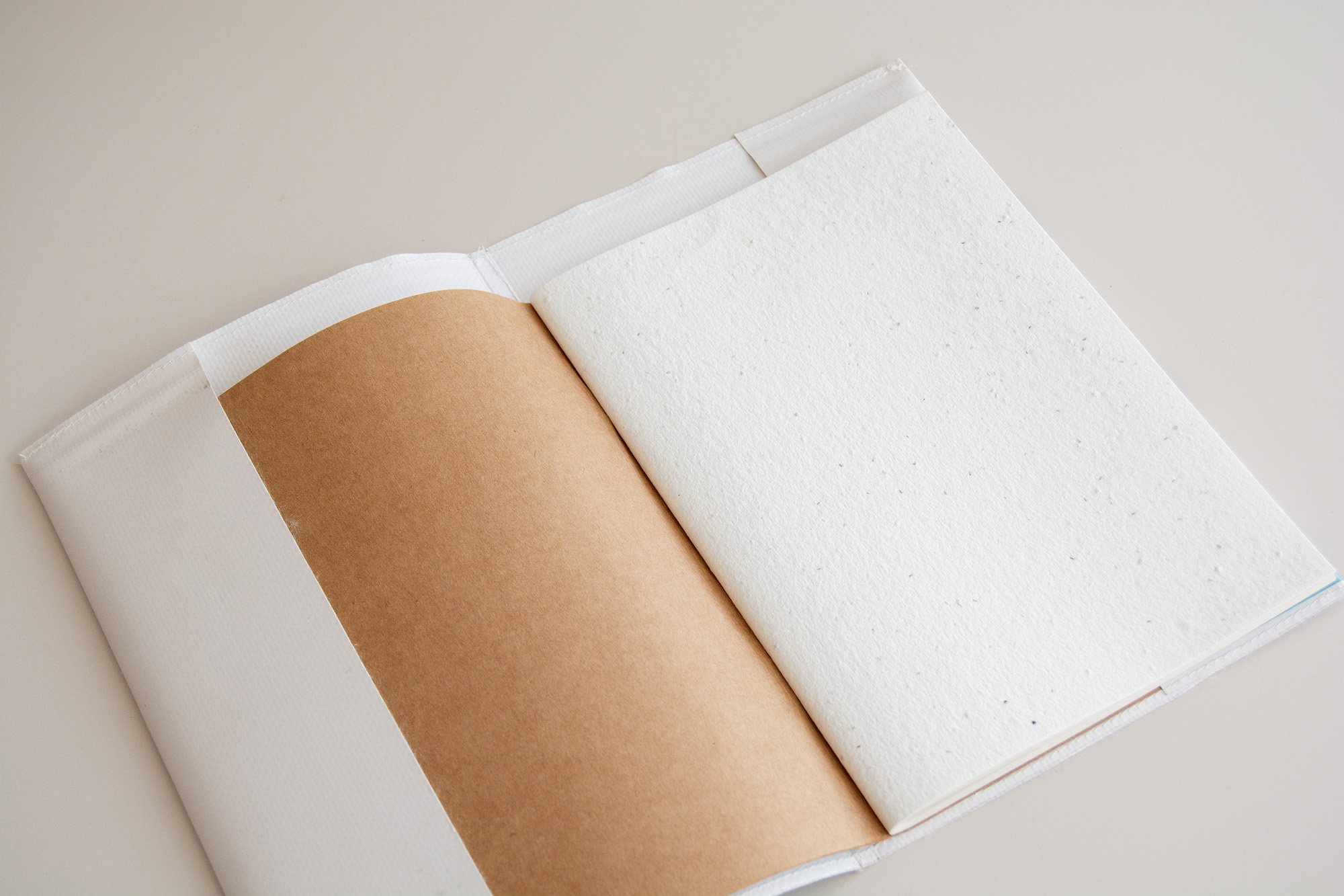 Mano sosteniendo libreta con grapas con diseño de abstracto y colores divertidos y espacio para añadir logotipo. Sobre fondo neutro.