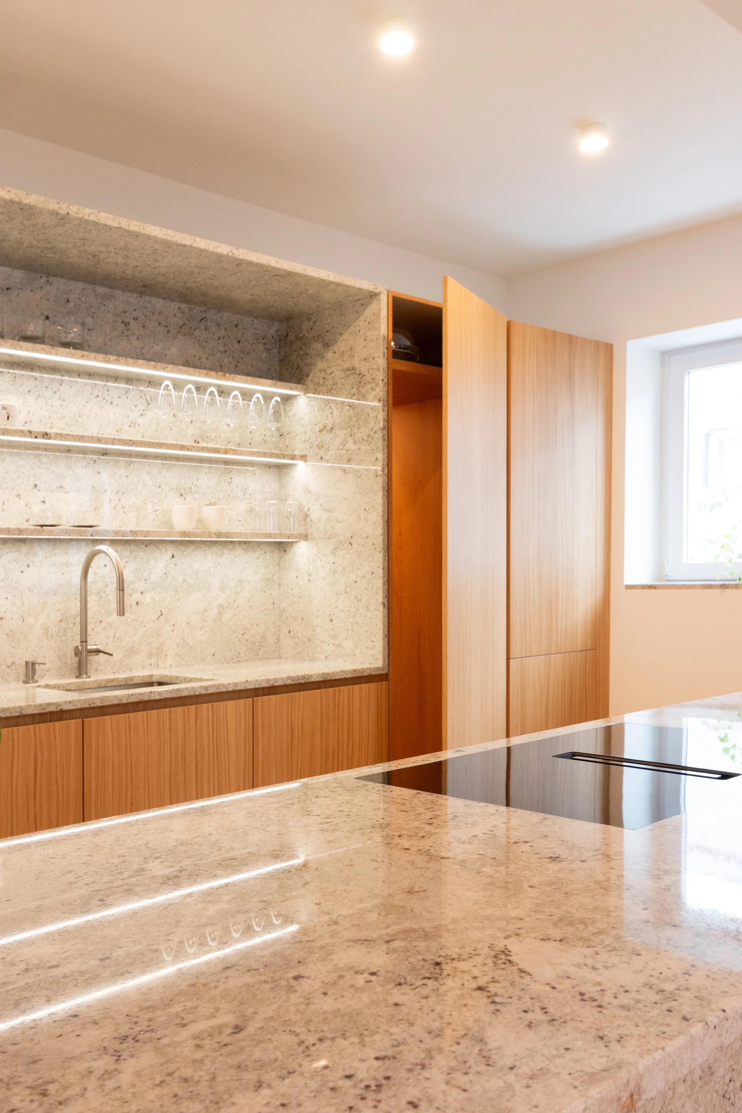 Modern kitchen with granite countertops, wooden cabinetry, and a window letting in natural light.