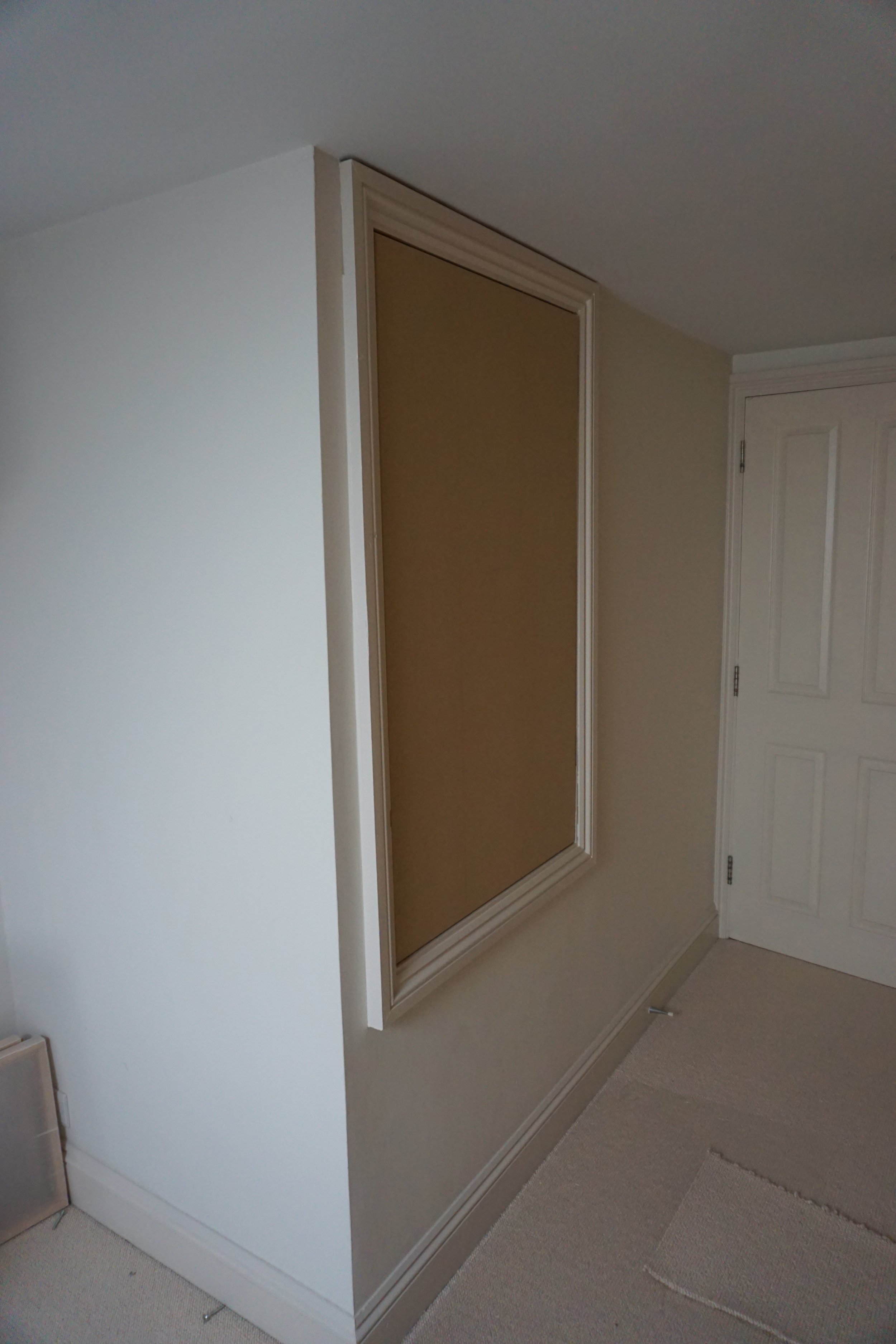 Interior corner of a room with a mirror on a beige wall, white door, beige carpets, and trim.