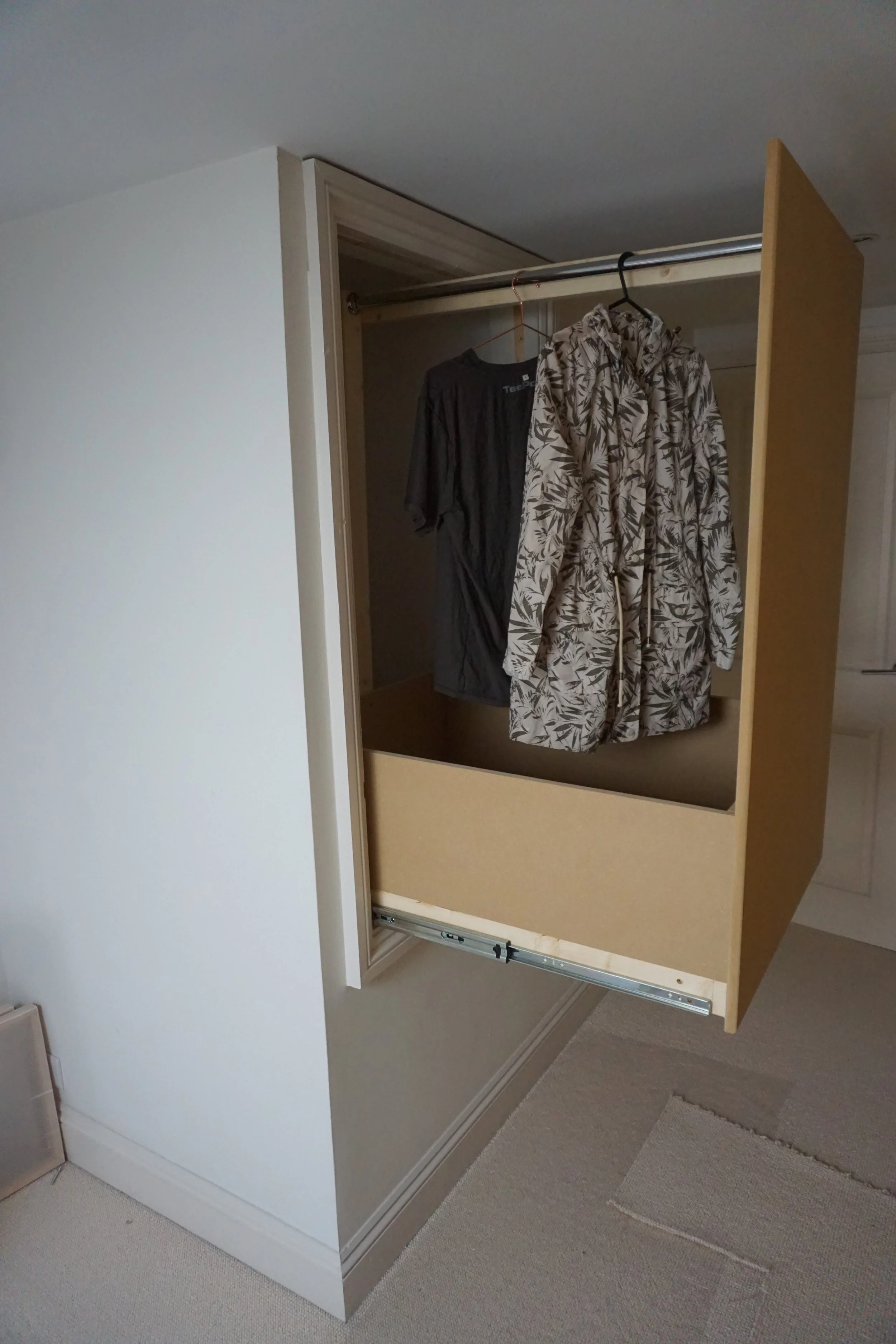 Open closet with two hangers holding a black T-shirt and a patterned jacket or coat, with sliding doors partially open.