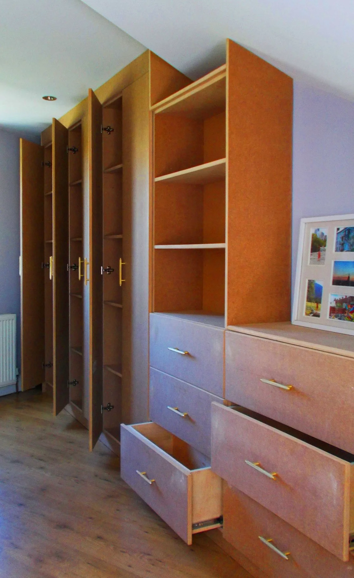 Wooden wardrobe with multiple open and closed drawers and shelves in a room with wooden flooring.