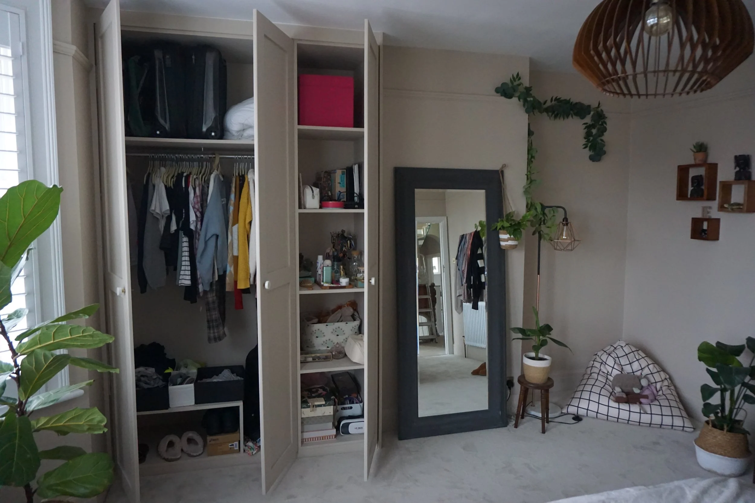 Bedroom with open closet, large mirror, plants, bean bag chair, and wall decor.