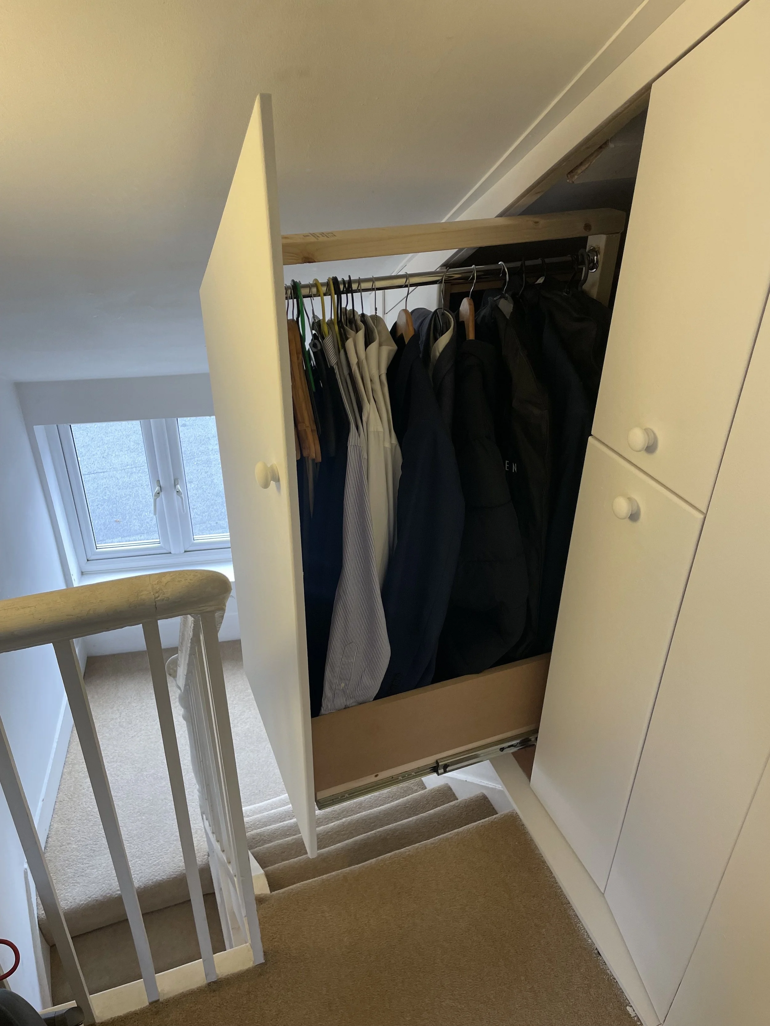 Pullout wardrobe on top of stairs containing hanging clothes