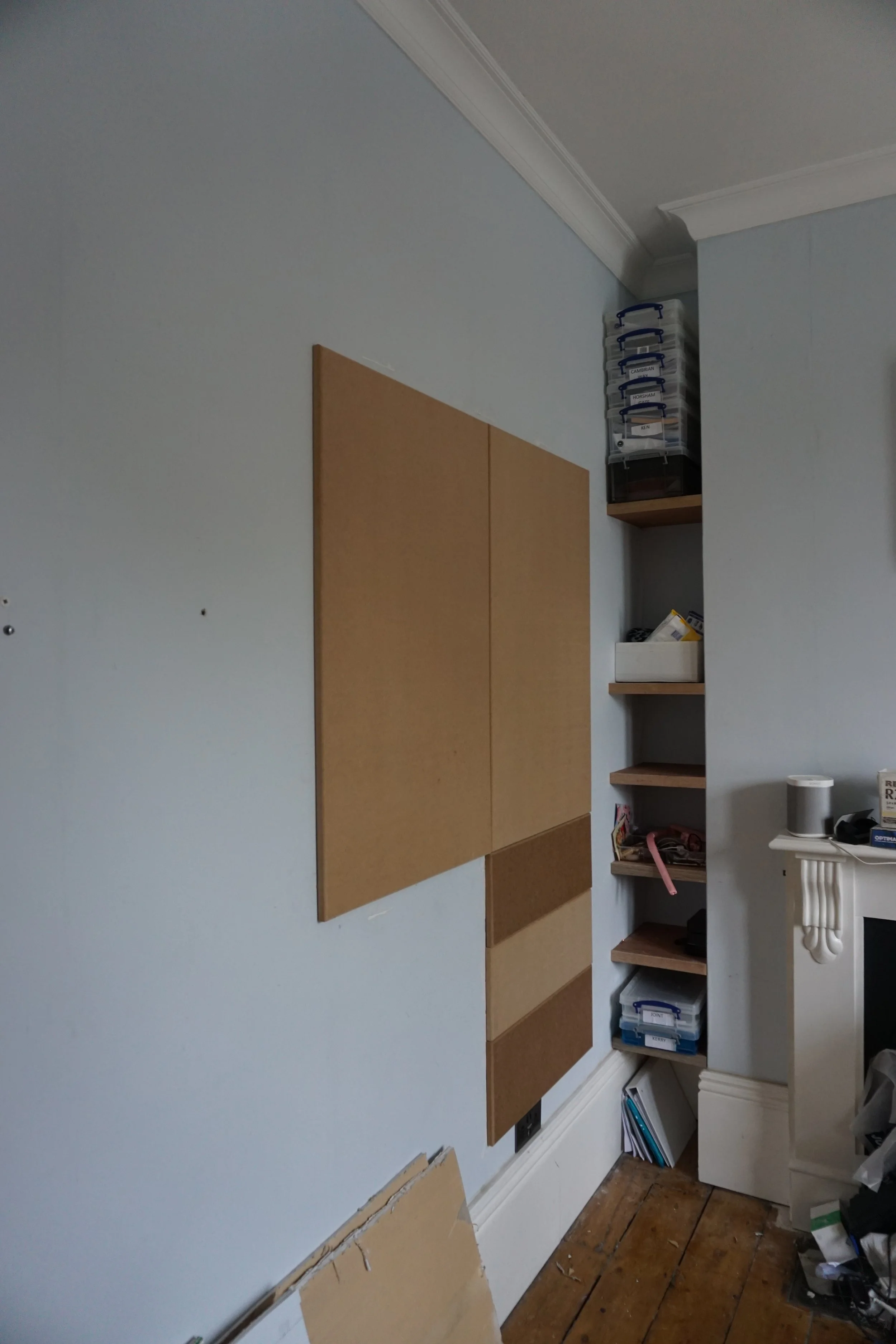 A partially decorated wall with corkboard squares, a small bookshelf, and a cluttered corner with office supplies.