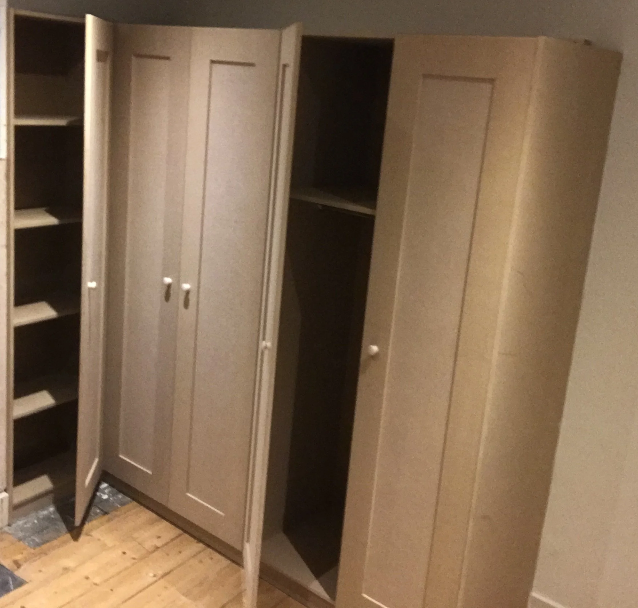 Open beige wooden closet with multiple shelves and hanging space, situated on a wooden floor.