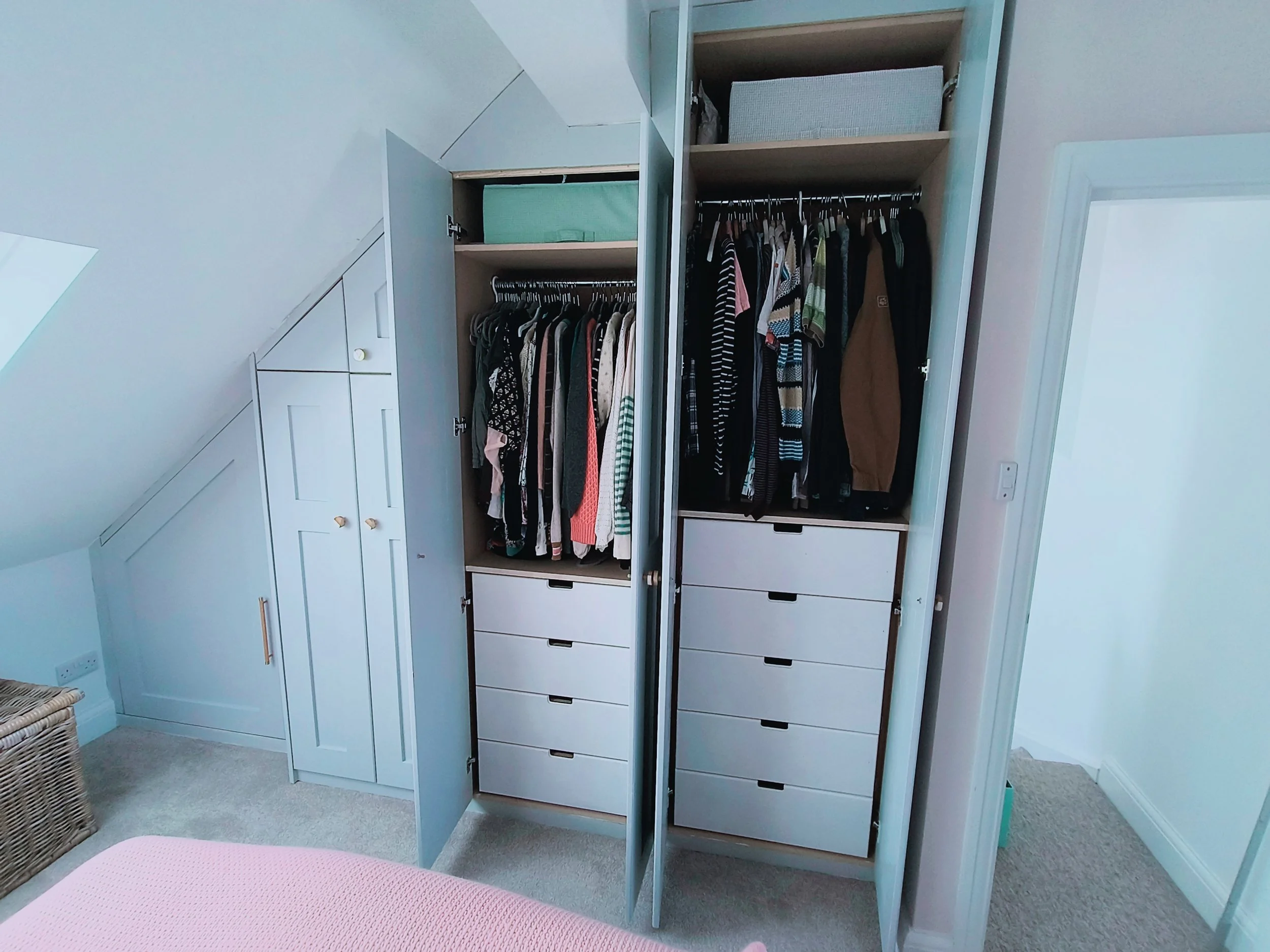 Open wardrobes filled with hanging clothes and drawers, with a sloped ceiling in the background.