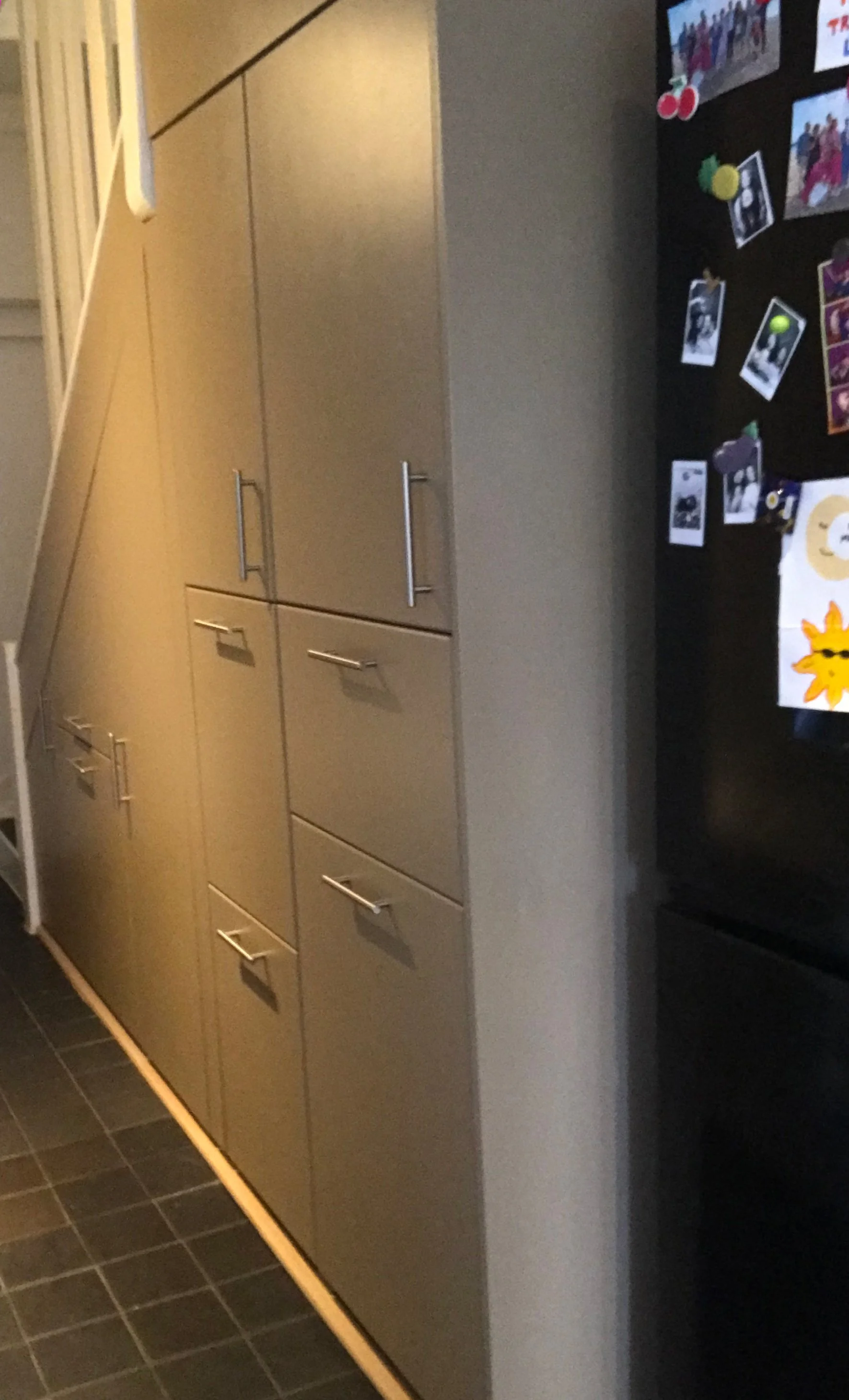 Kitchen with beige cabinets, black tile floor, and a refrigerator covered with colorful magnets and photos.