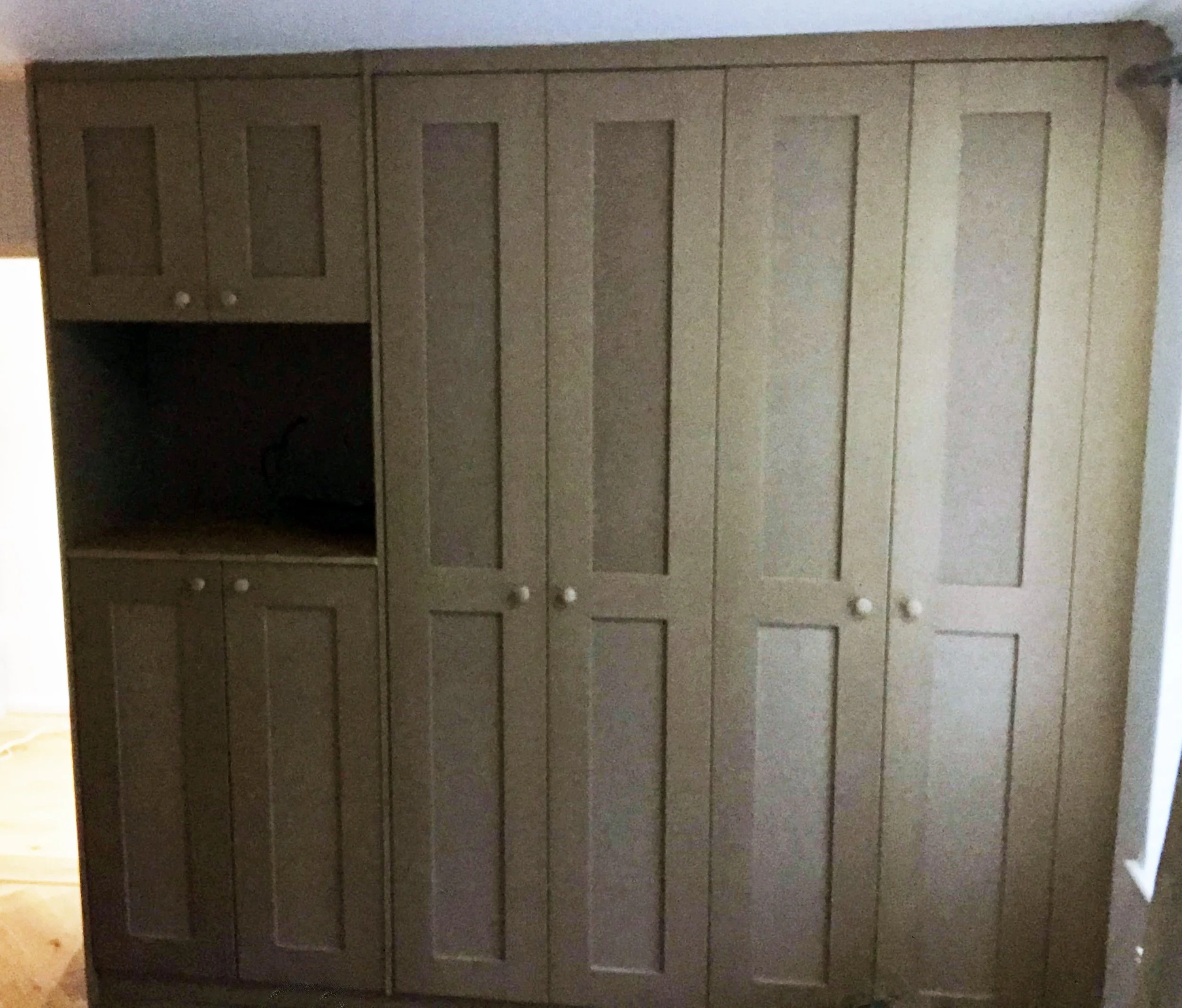 A large built-in wardrobe with multiple doors, made of light-colored wood, in a room with hardwood flooring.