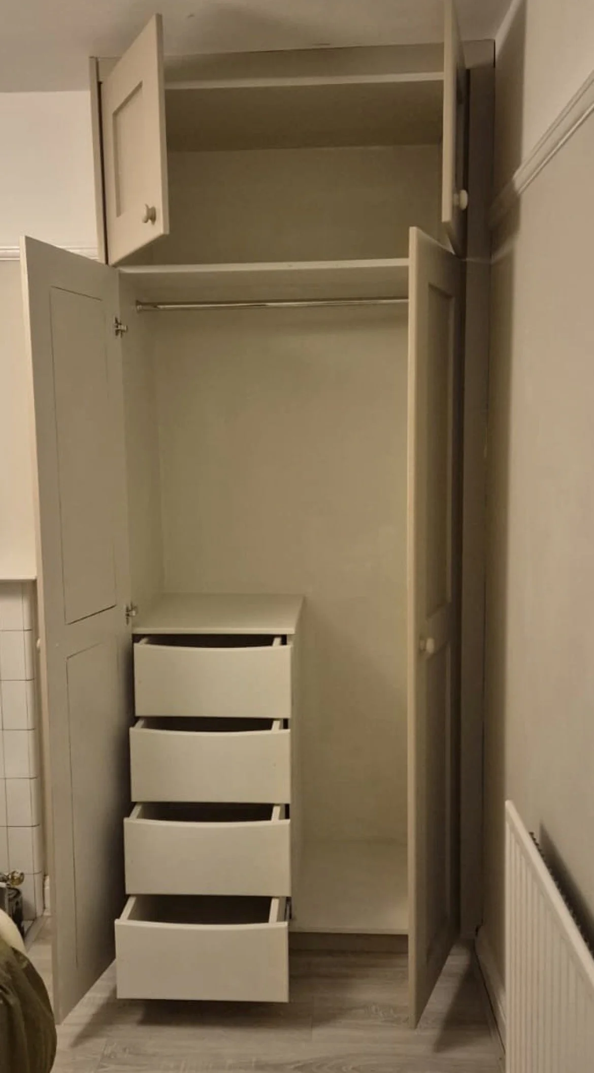 Open white wardrobe with multiple empty shelves and a set of five white drawer units inside.