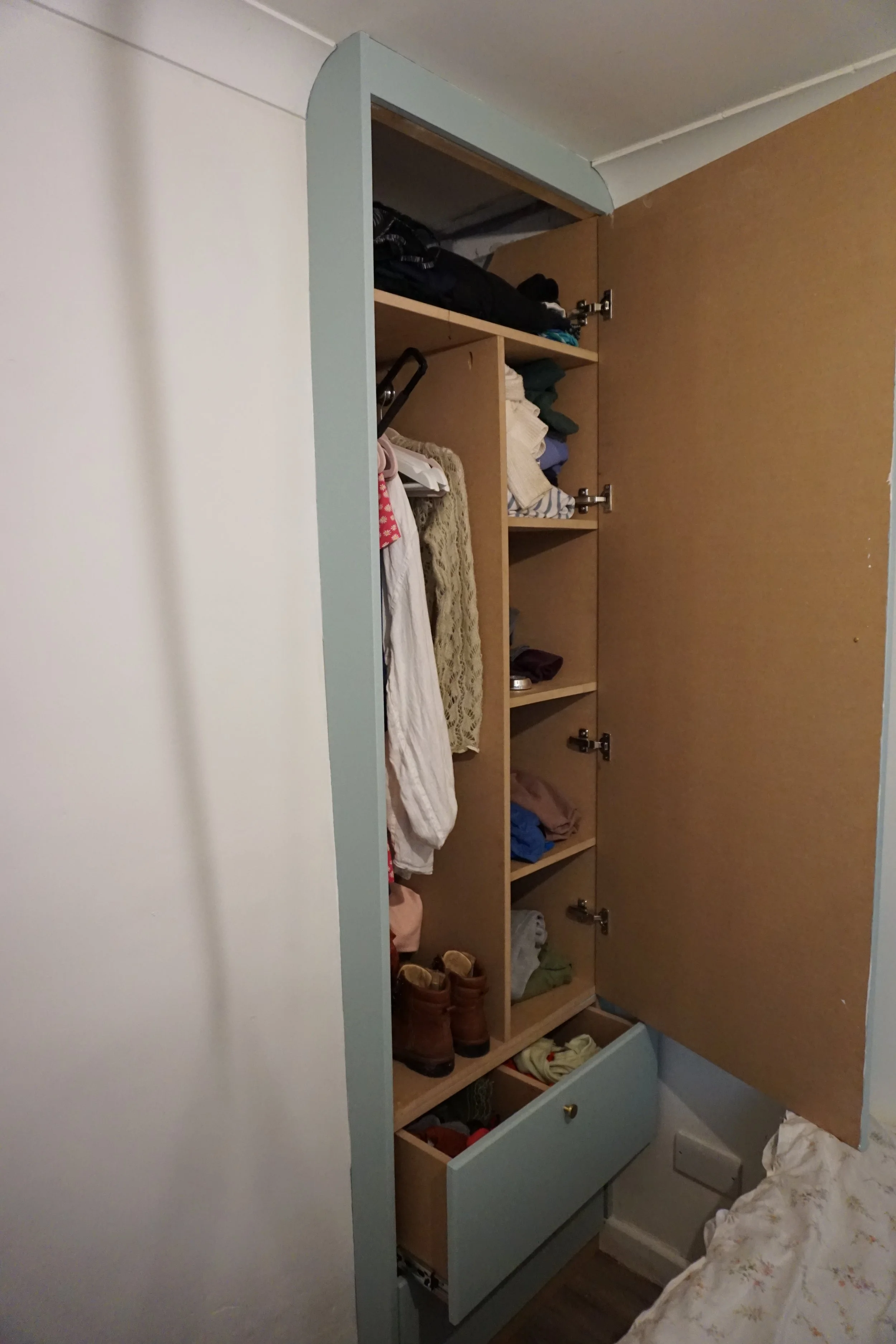 Open wardrobe with hanging clothes, folded clothes on shelves, and boots inside.