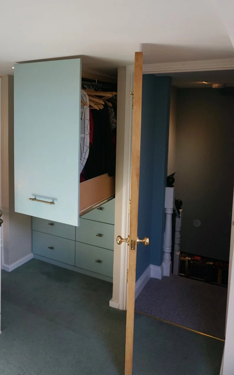 Open closet door revealing hanging clothes and drawers inside a bedroom closet.