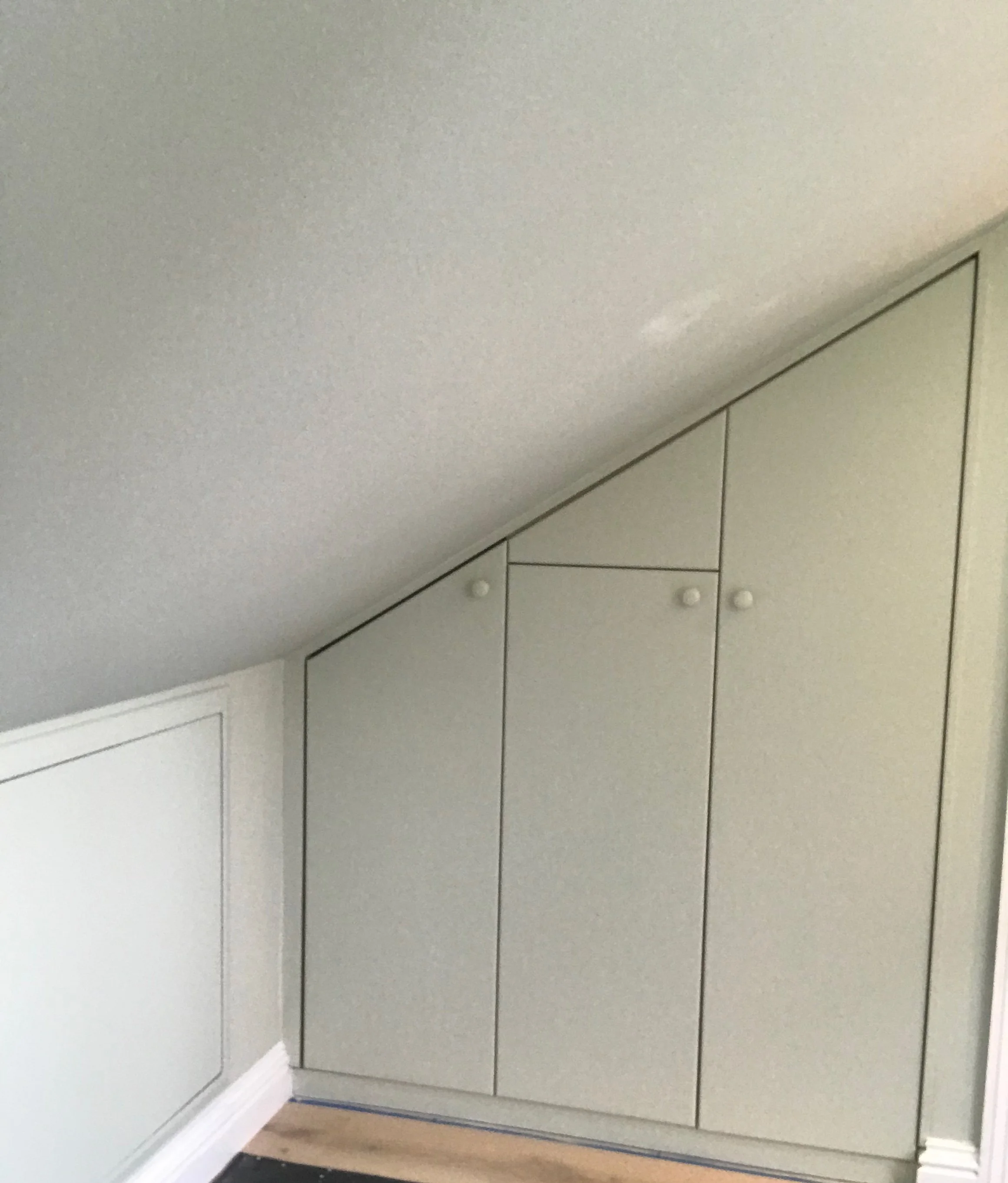 Built-in beige cabinets with black outlines under a sloped ceiling in a room.