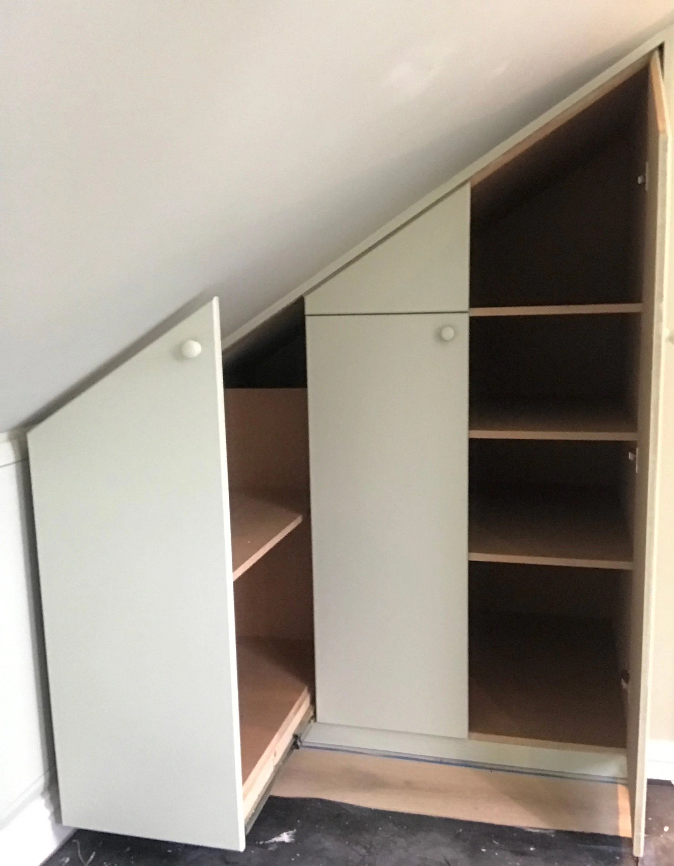 A modular storage unit with white and wooden doors and open shelves, designed to fit under a sloped ceiling.