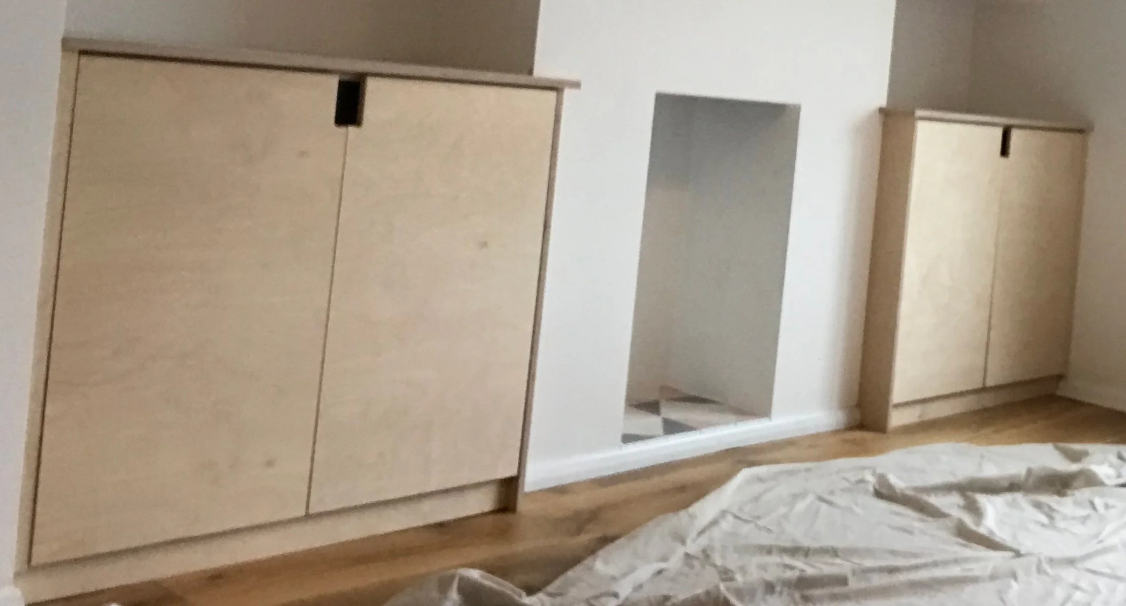 Wooden cabinets against a white wall in a room with a sheet on the floor