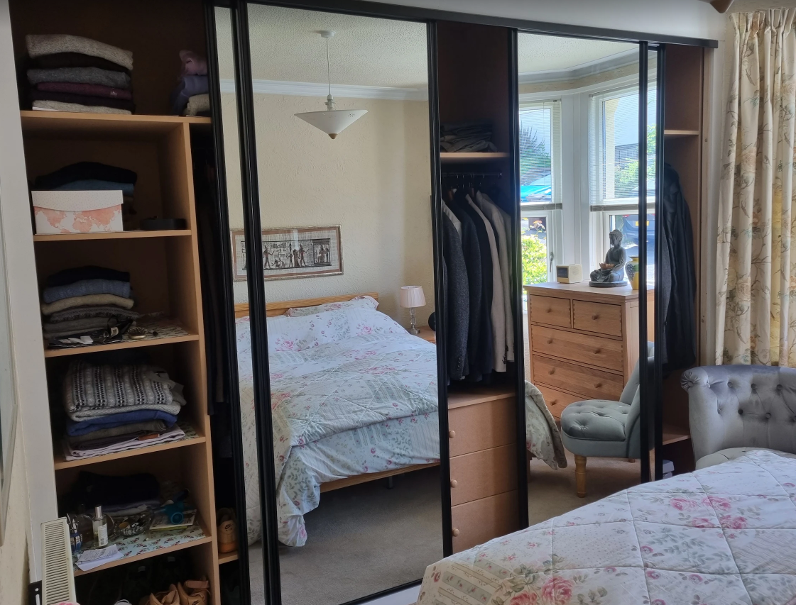 Mirror wardrobes and fitted shelves with doors open in bedroom