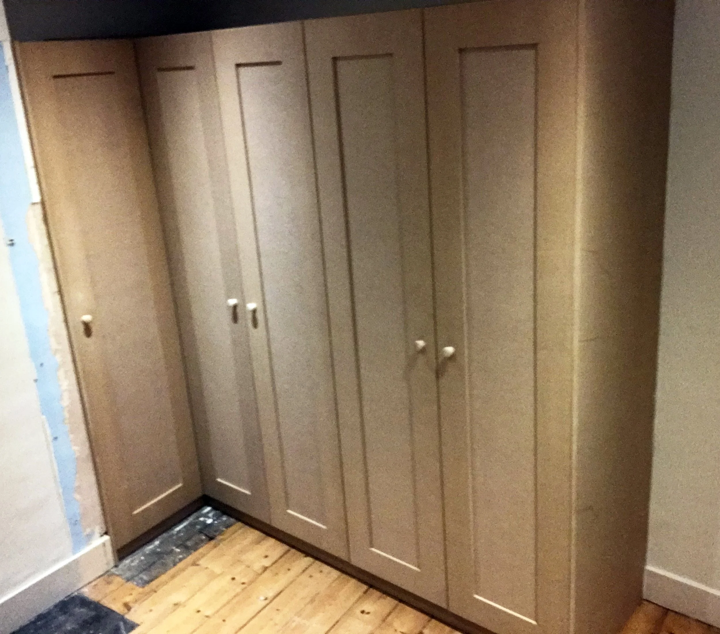 Wooden built-in closet with multiple doors in a room with wood flooring.