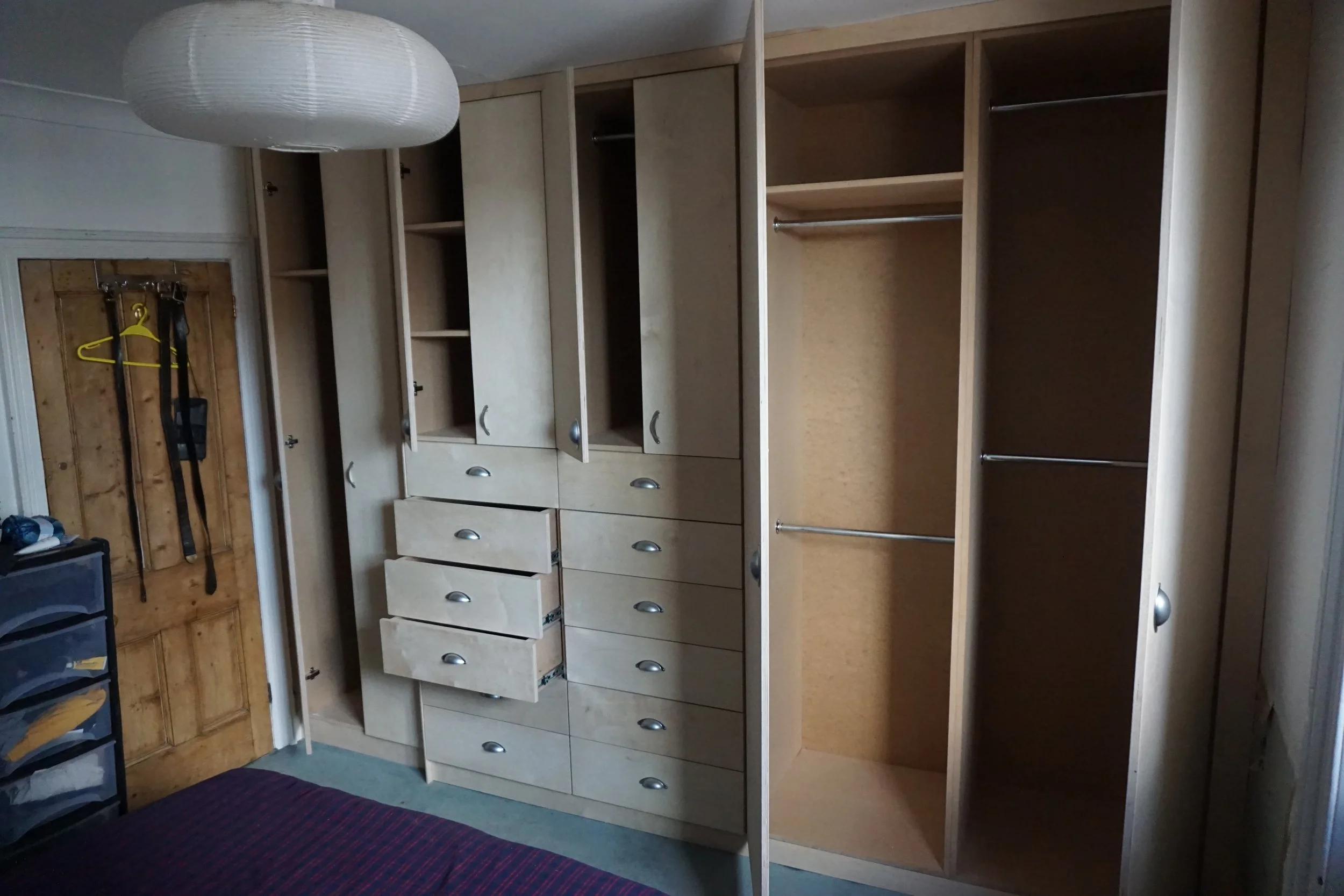 Open empty wooden closet with multiple shelves and drawers in a bedroom.