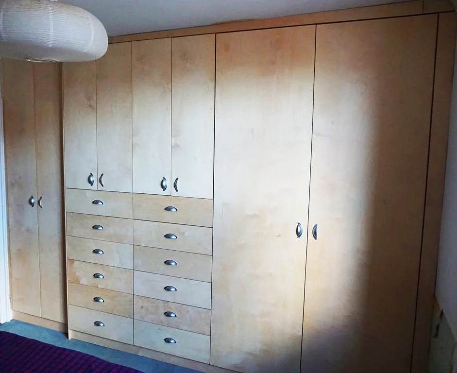 Built-in wooden wardrobe with multiple doors and drawers in a bedroom.