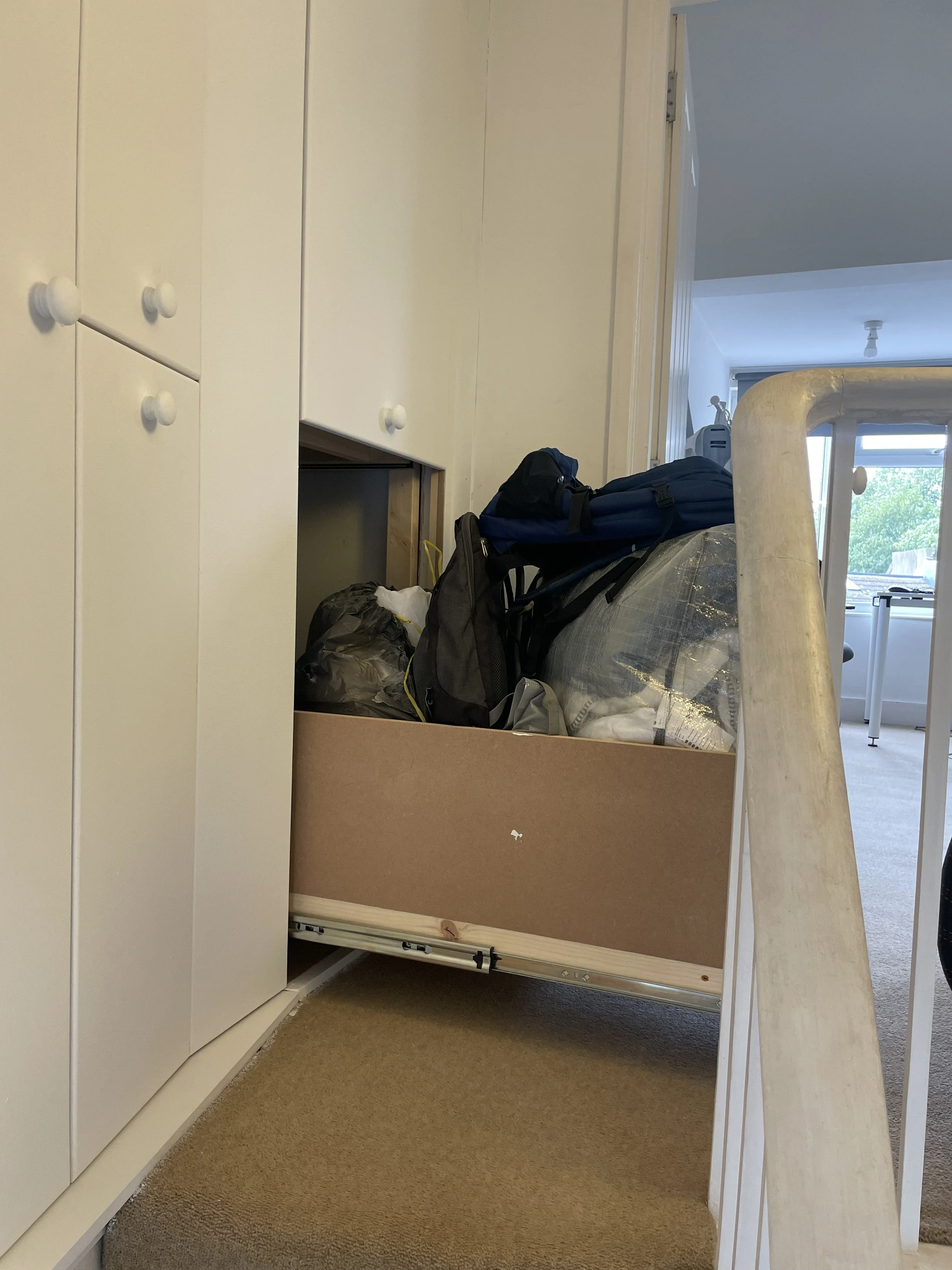 A partially open cabinet drawer filled with bags, backpacks, and miscellaneous items in a home interior.