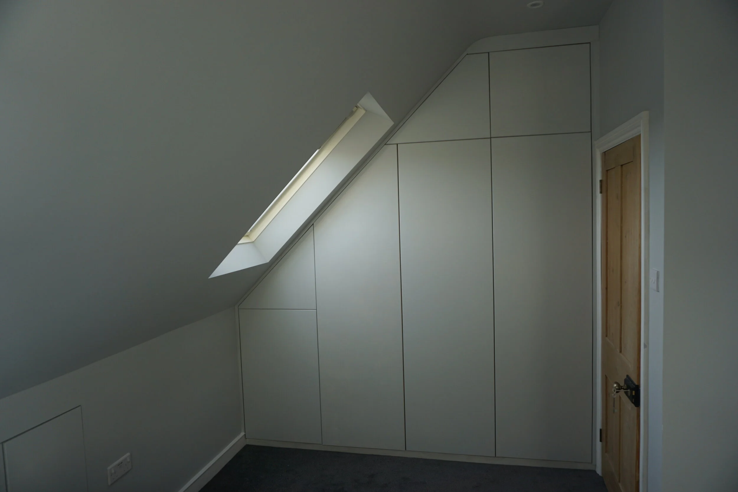 Room with sloped ceiling and built-in white storage cabinets, a skylight window, and a wooden door.